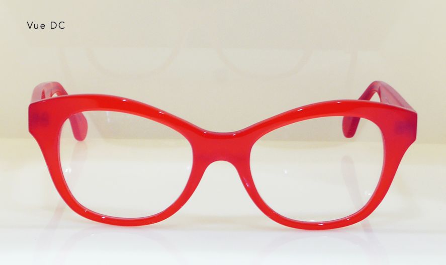 Red-framed eyeglasses with clear lenses resting on a white surface.