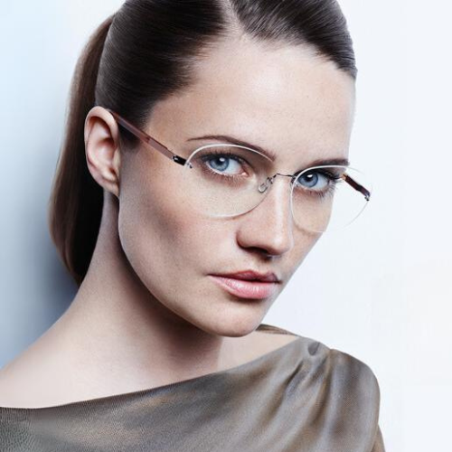 Woman wearing rimless eyeglasses, looking forward, ponytail, neutral expression.