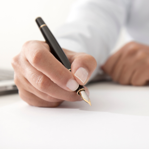 Hand holding a black fountain pen, writing on white paper.