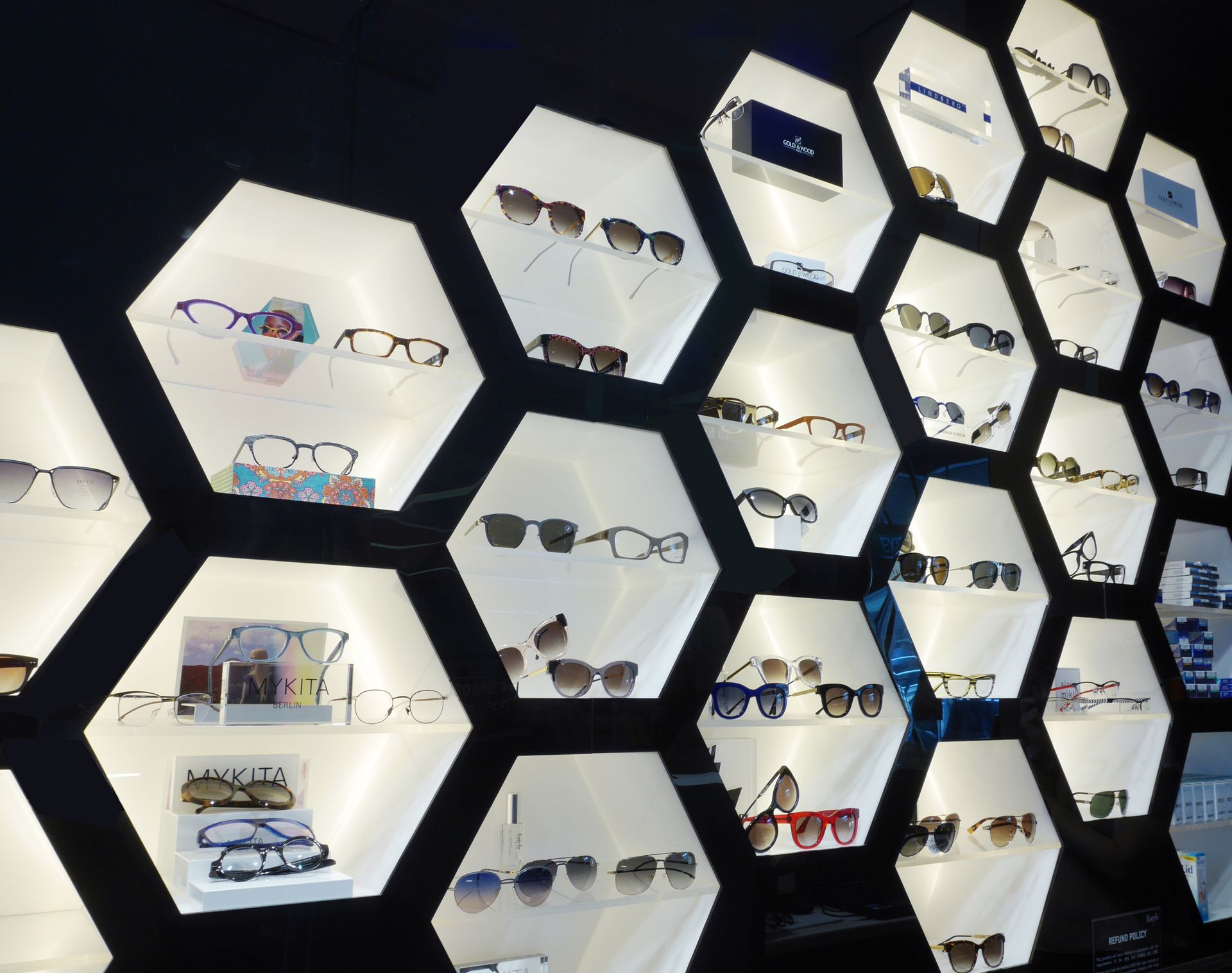 Eyeglass display with illuminated honeycomb shelves. Various frames are showcased.