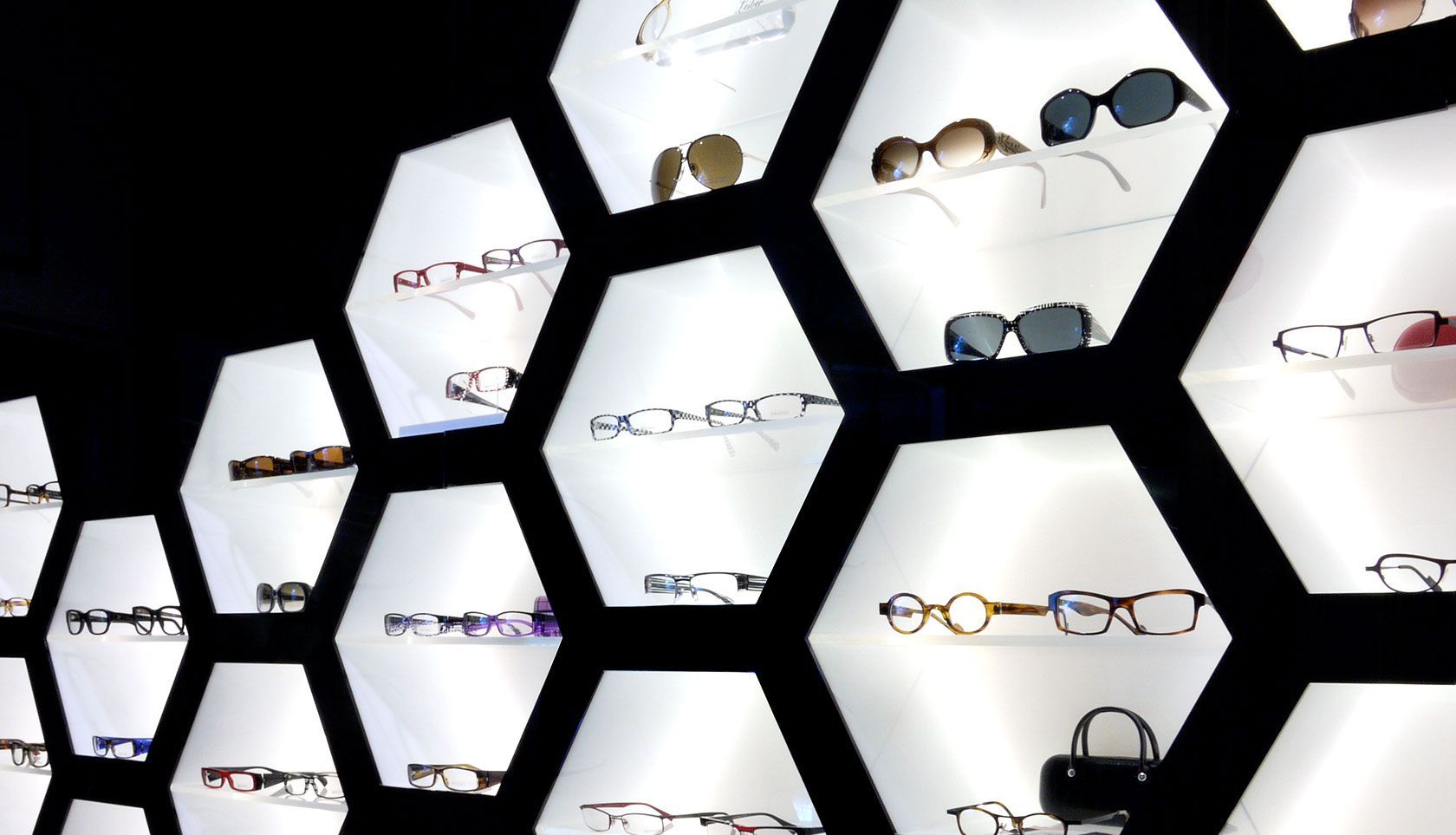 Wall display of eyeglasses in illuminated hexagonal shelves.