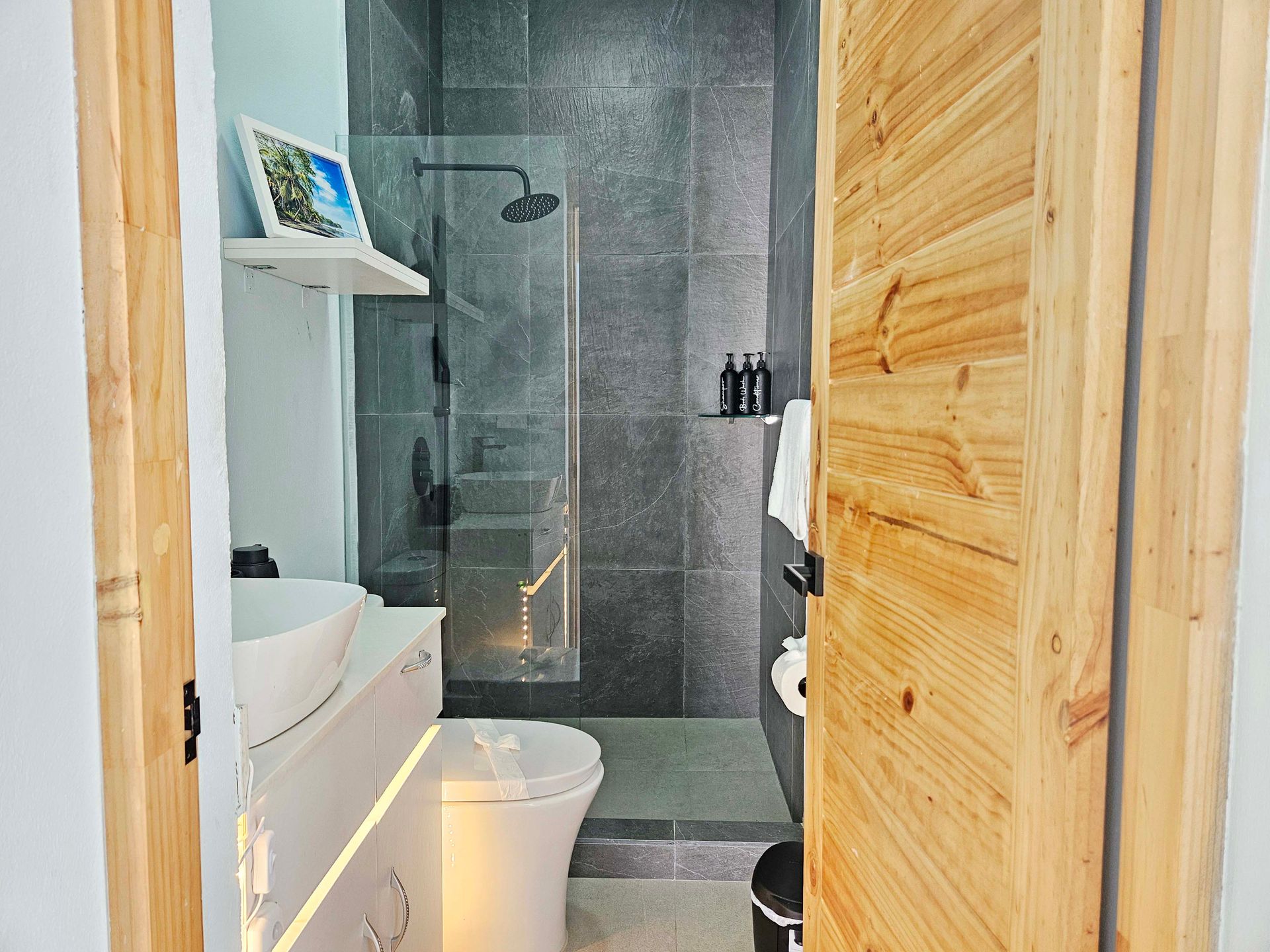 Bathroom interior with wooden door, gray tile shower, white sink, and toilet.