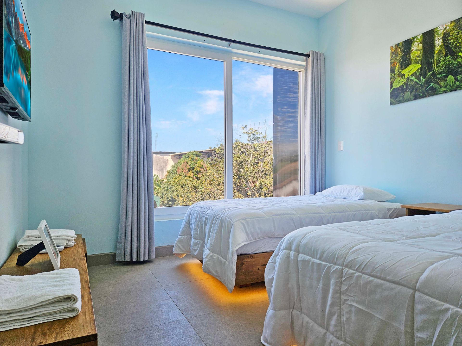 Bedroom with two beds, window with view, TV, and light blue walls.