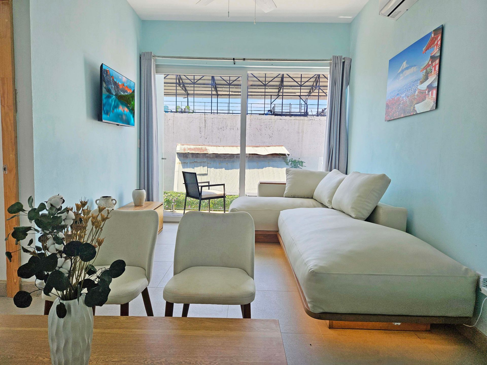 Living room with white sofa, chairs, and sliding glass door to outdoor space. Light blue walls and artwork.