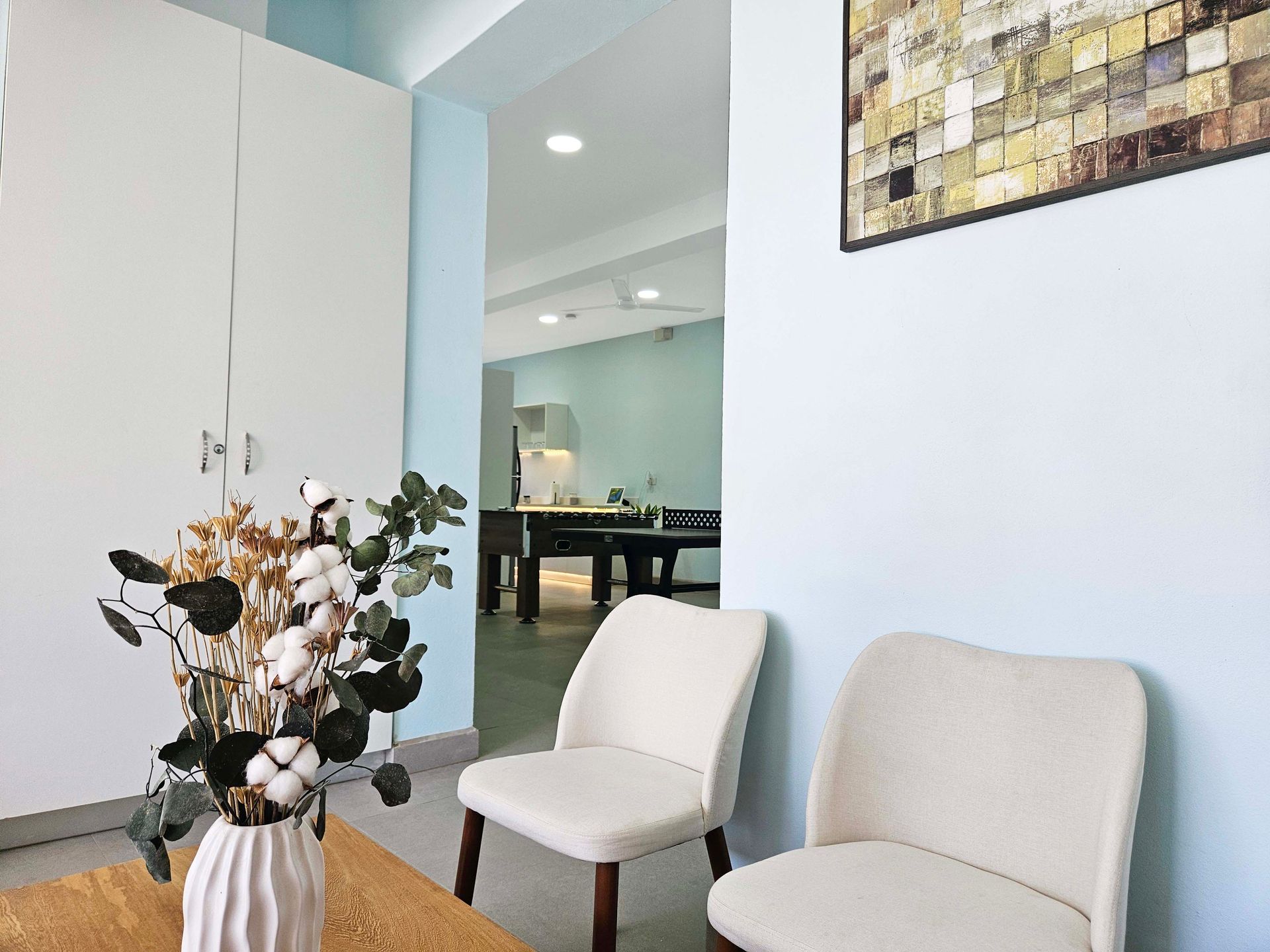Two cream chairs in a light blue room, with a floral arrangement in front of a doorway.