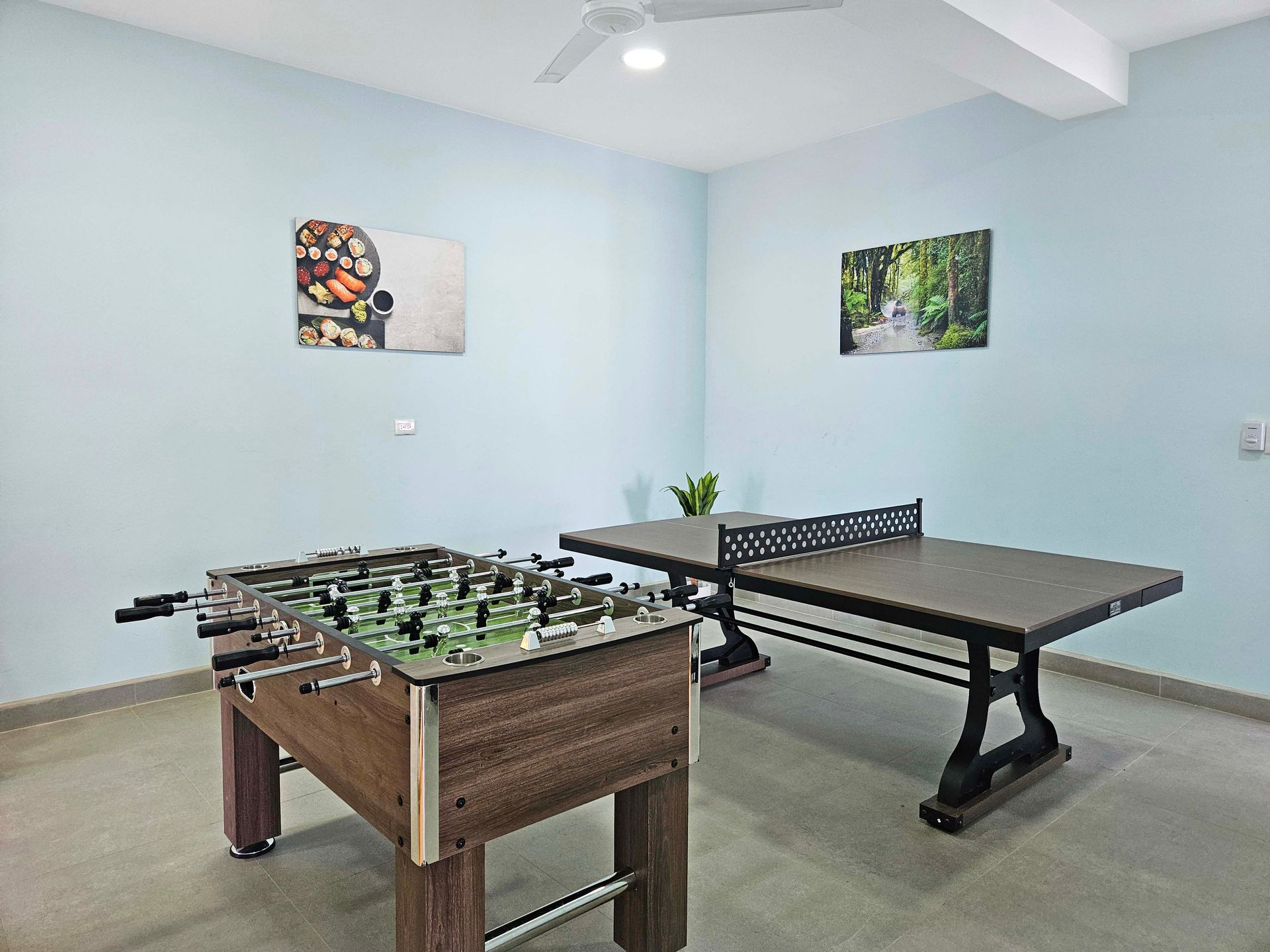 Foosball and ping pong tables in a room with blue walls and two framed pictures.