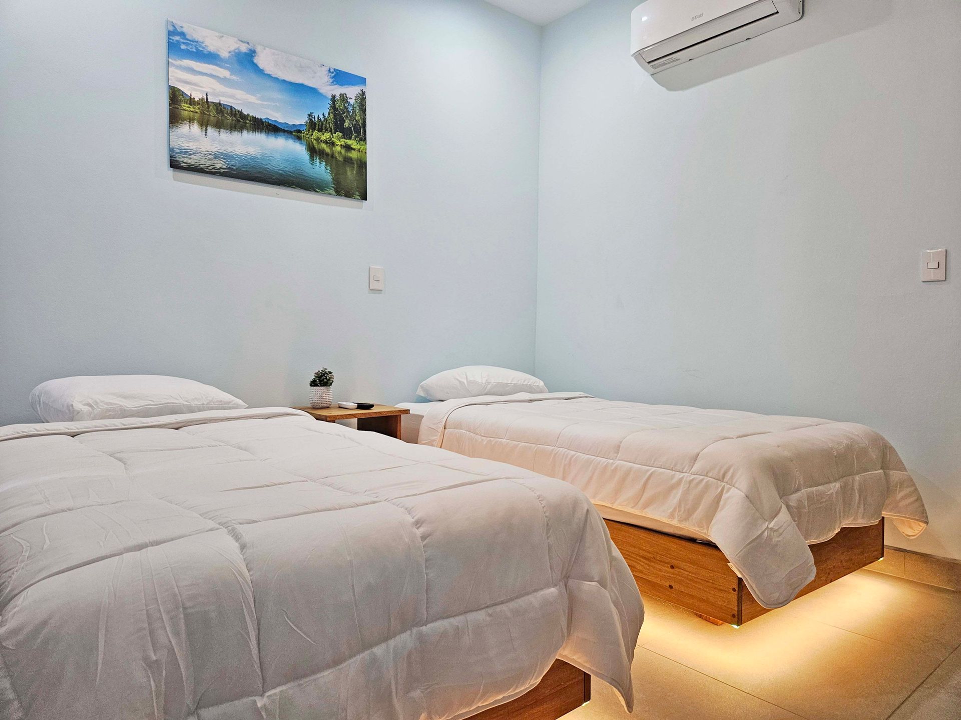 Bedroom with two twin beds, white bedding, light blue walls, art, and air conditioning.