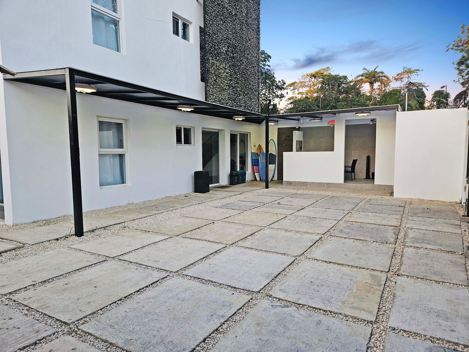 Outdoor patio with square stone tiles, white walls, and a black awning. Two people stand near a doorway.
