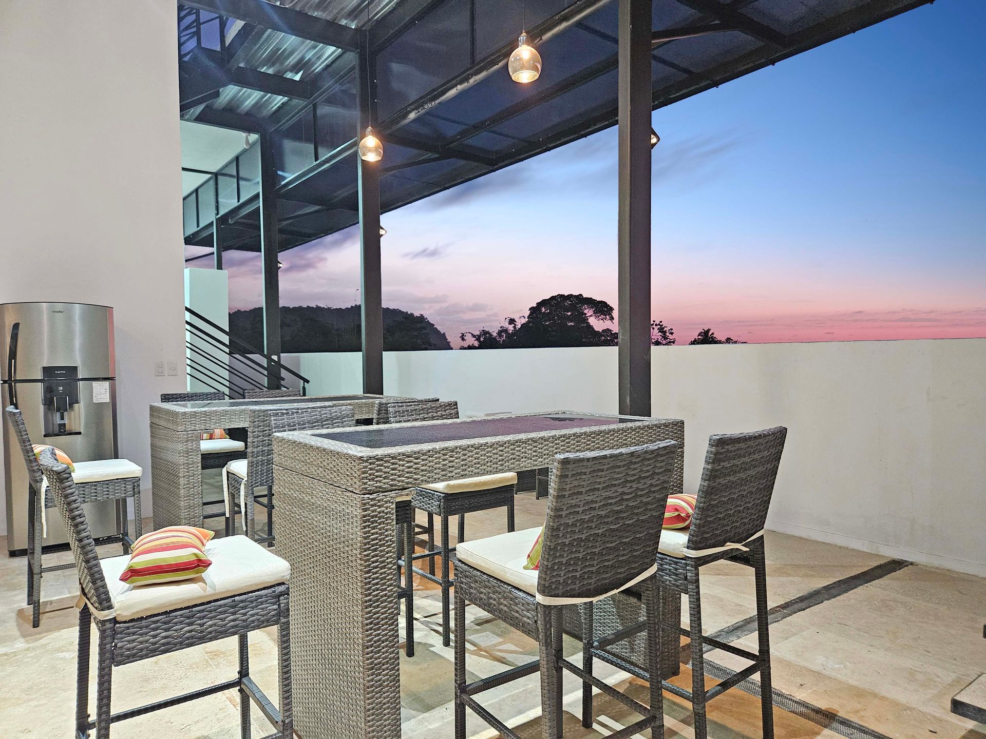 Outdoor patio with wicker bar stools and tables at dusk.