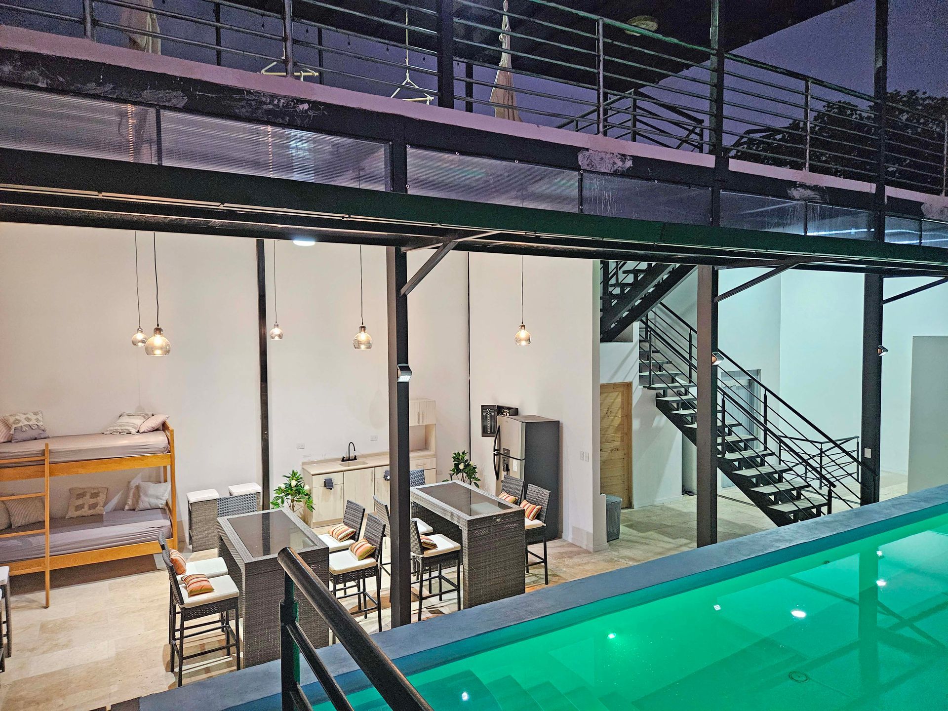 A modern indoor pool area with bunk beds, tables, and a staircase. Green pool water.