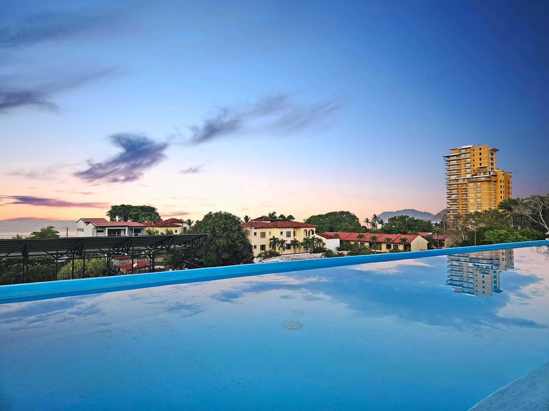 Infinity pool with city skyline at dusk; calm, blue water reflects buildings and sky.