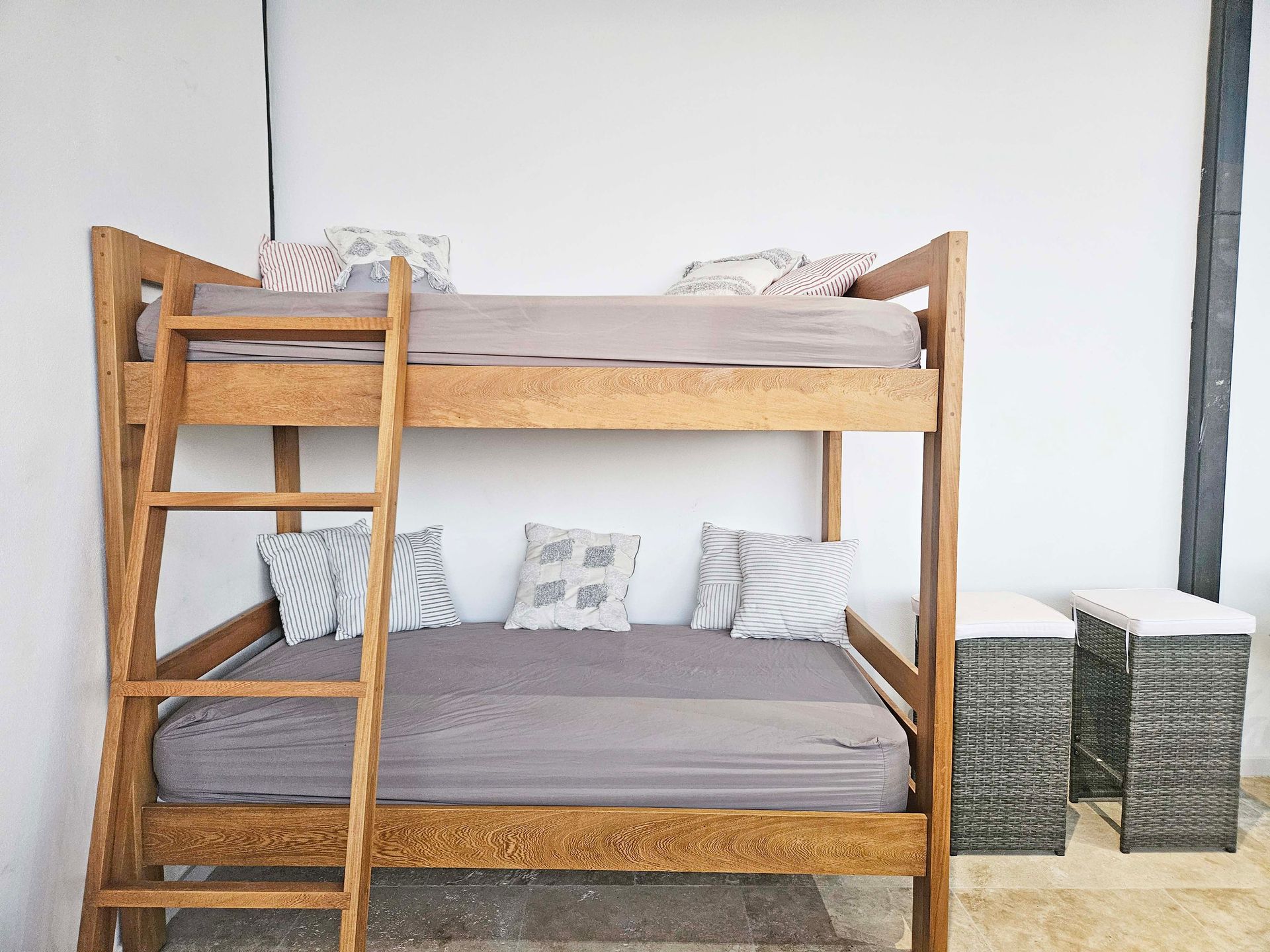 Wooden bunk bed with gray bedding and pillows, next to two small wicker tables.