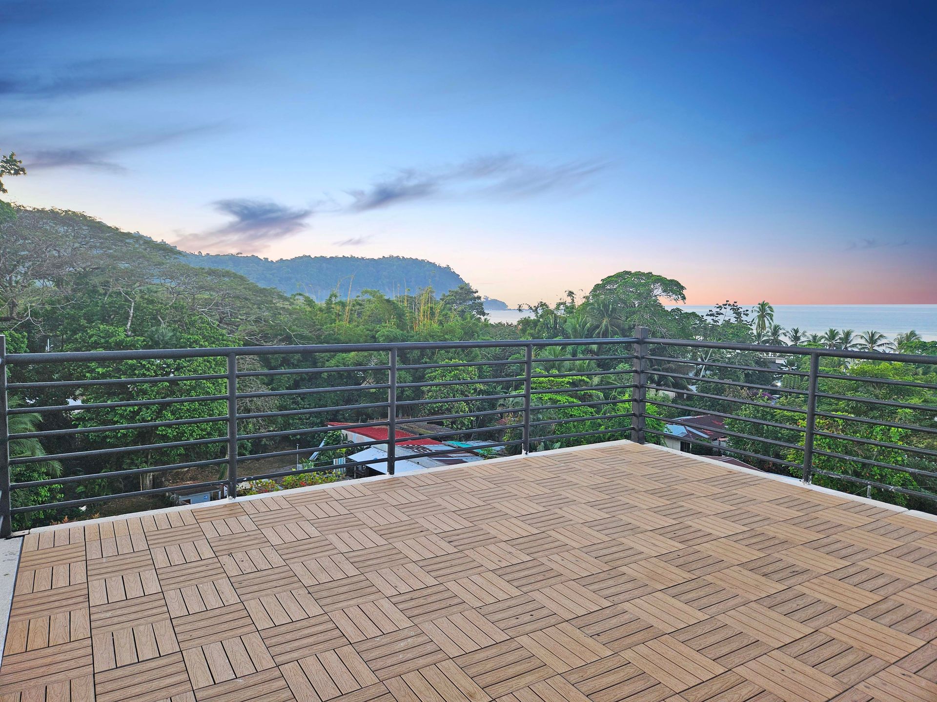 Balcony overlooking lush trees and ocean, with a blue sky.