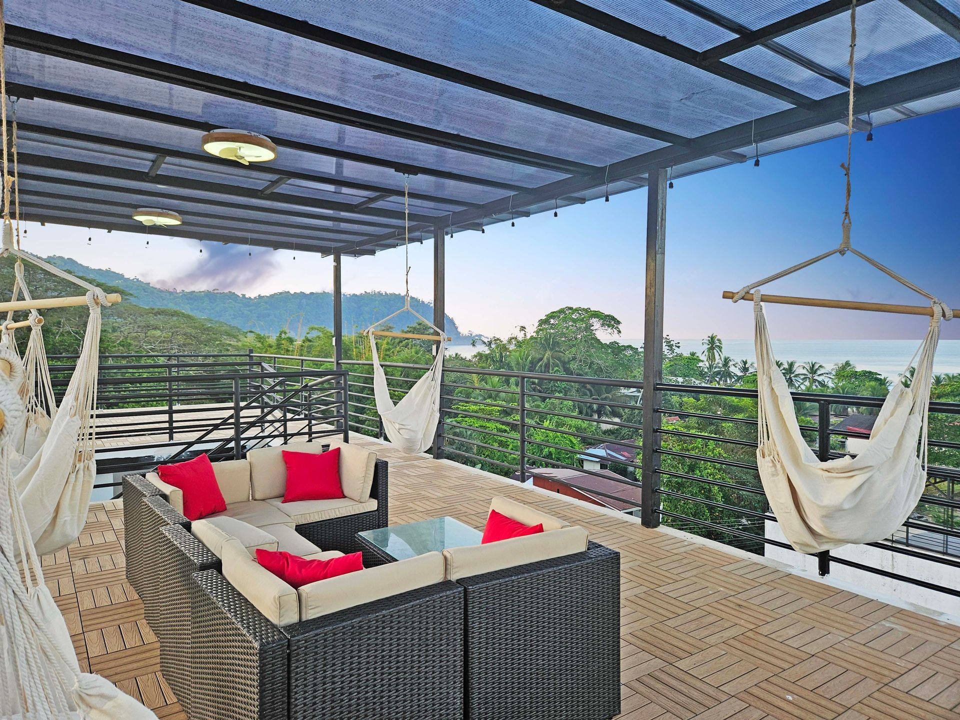 Rooftop deck with seating, hammocks, and ocean view. Black wicker furniture with red cushions under a canopy.