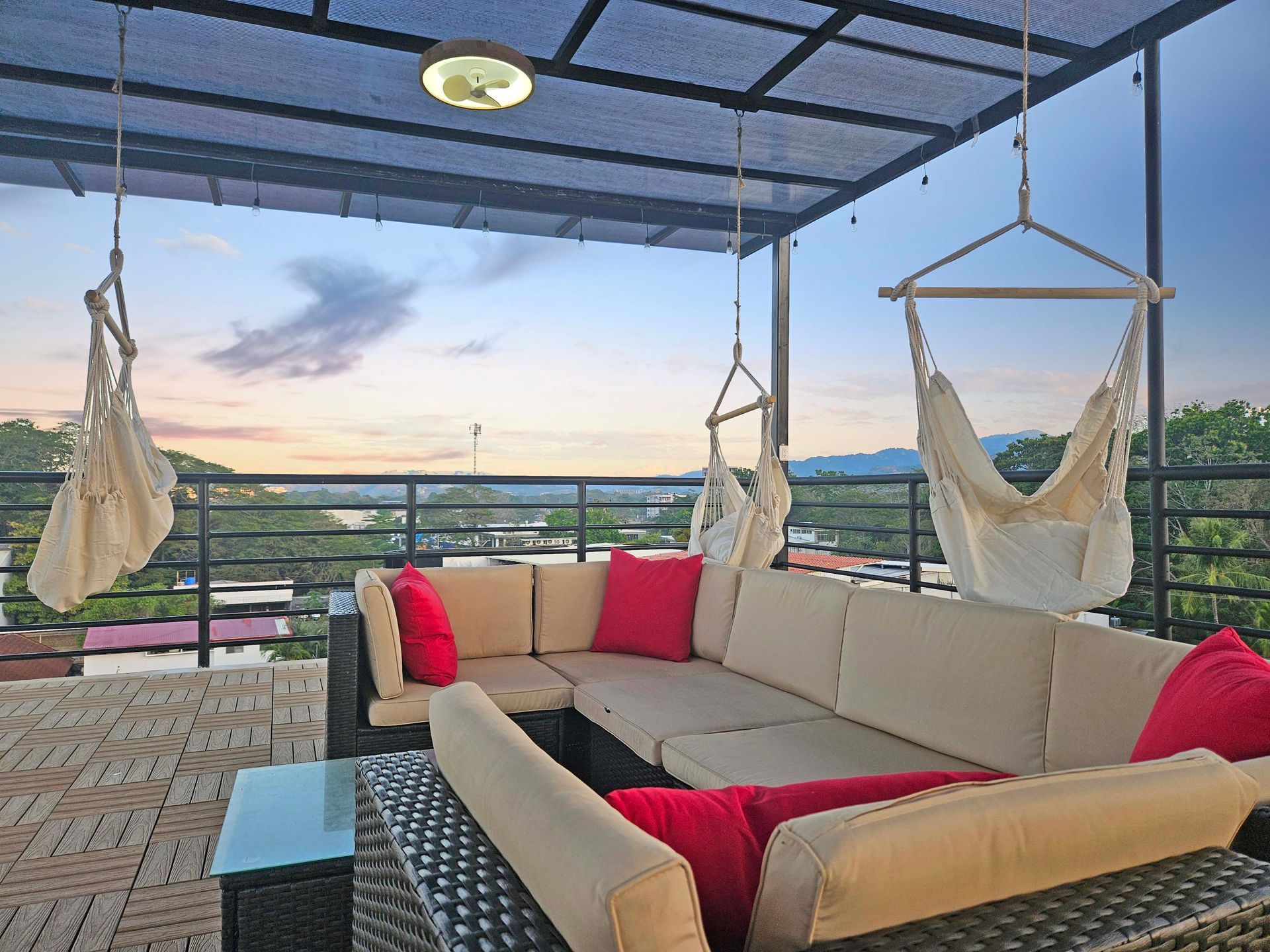 Rooftop deck with sectional sofa, hanging chairs, and scenic view at dusk.