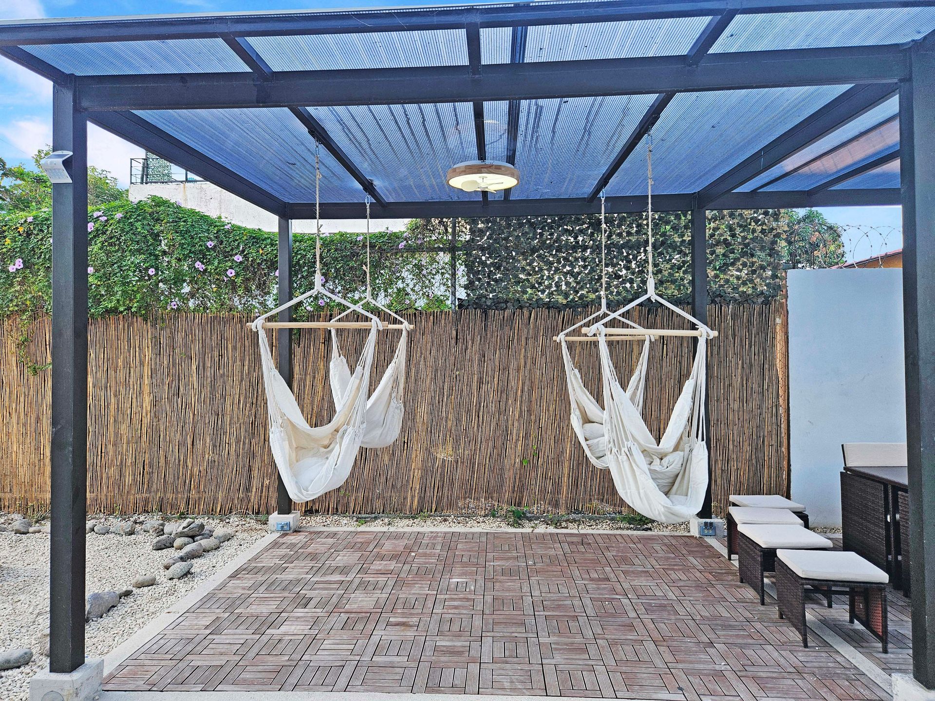 Patio with hammock chairs under a pergola, brown tiled floor, and a woven fence backdrop.