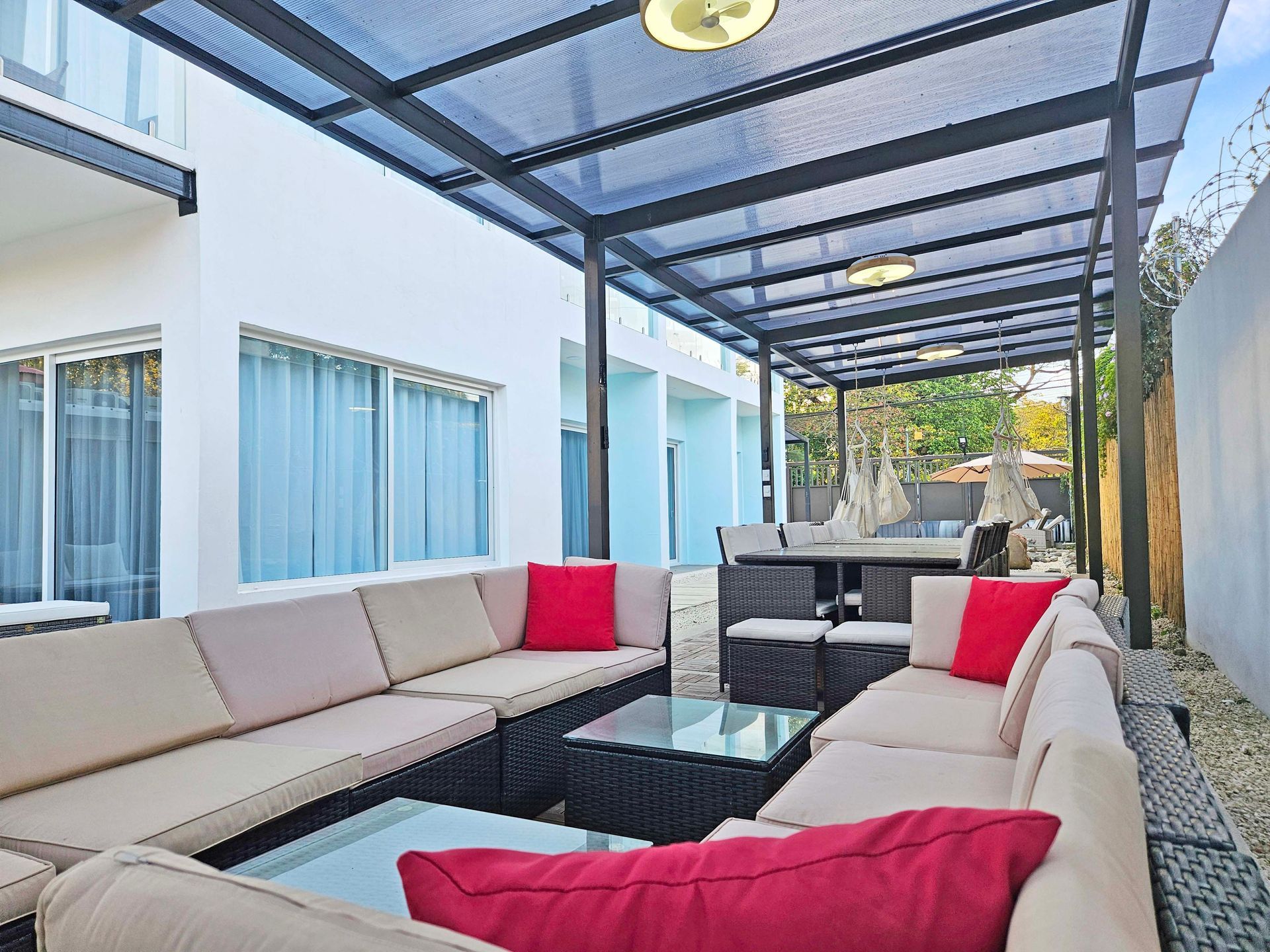Outdoor patio with beige sectional seating, red pillows, glass coffee table, and overhead canopy.