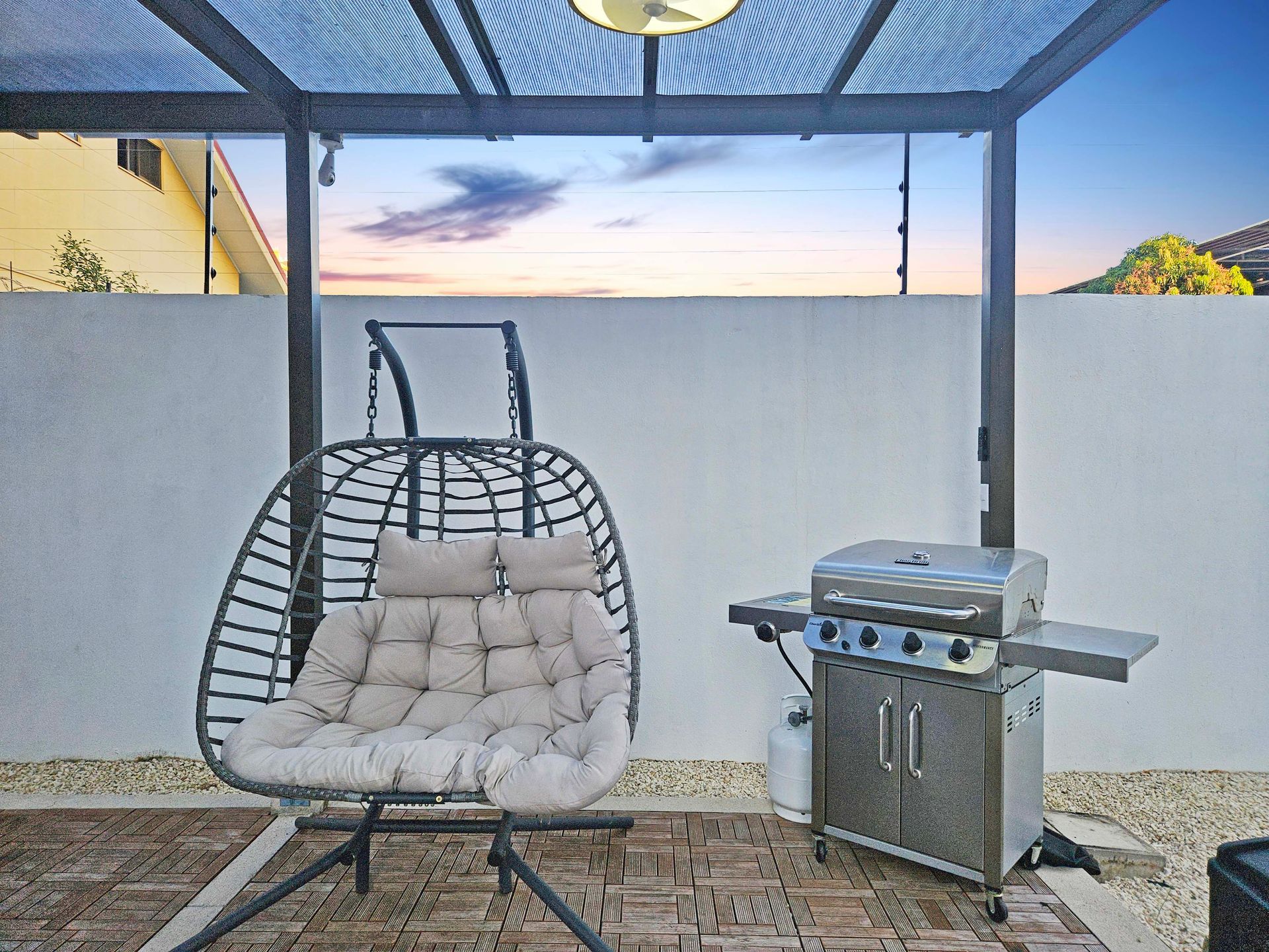 Patio with hanging chair, grill, pergola, and evening sky.