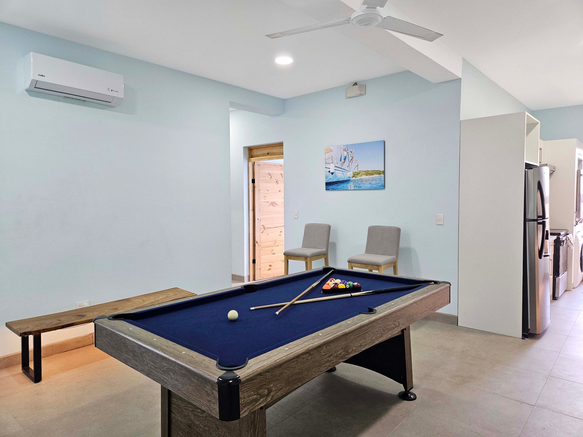 Pool table in a light blue room with a bench, chairs, and a painting.