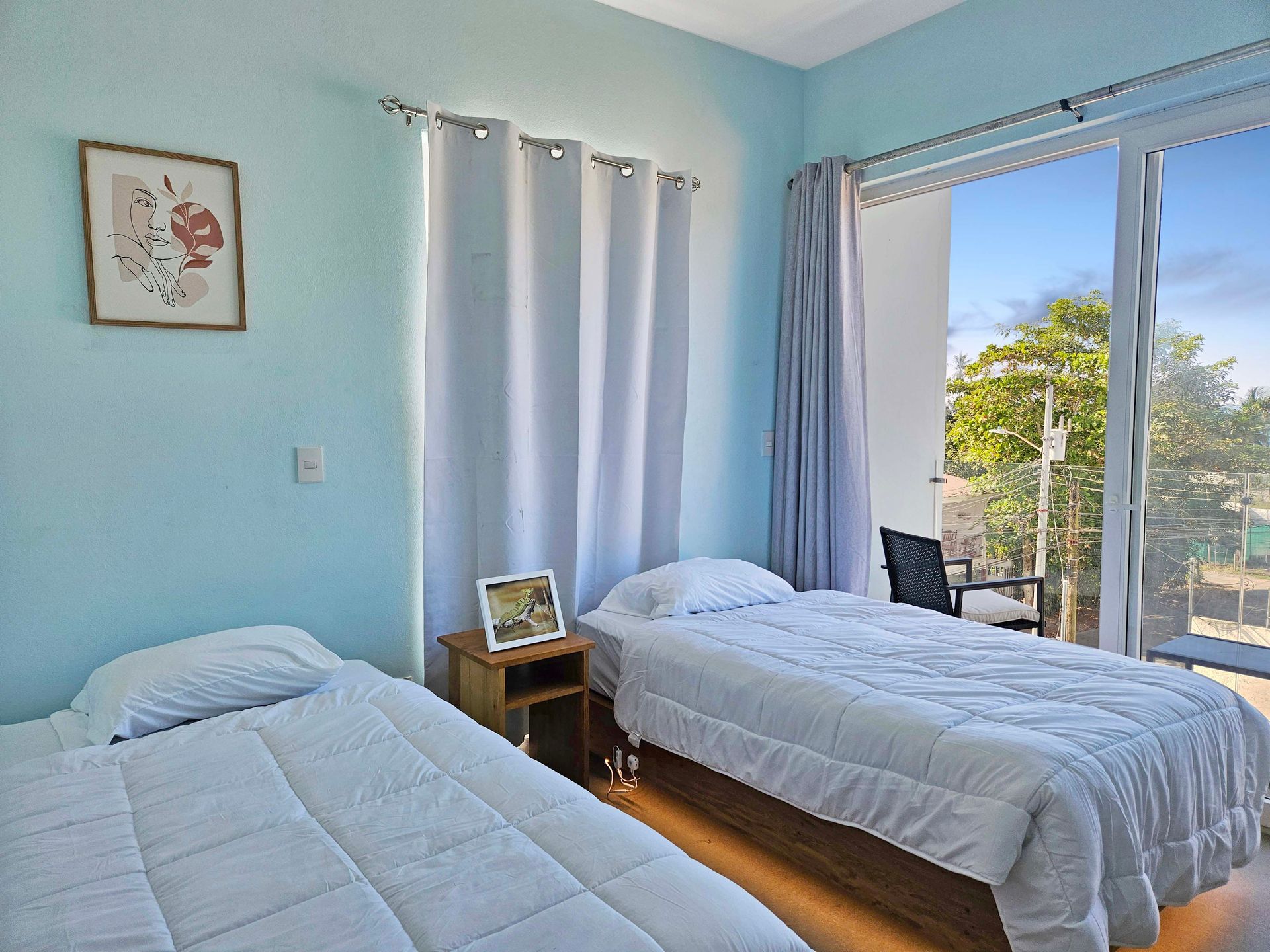 Two twin beds in a room with light blue walls, a window, and artwork.