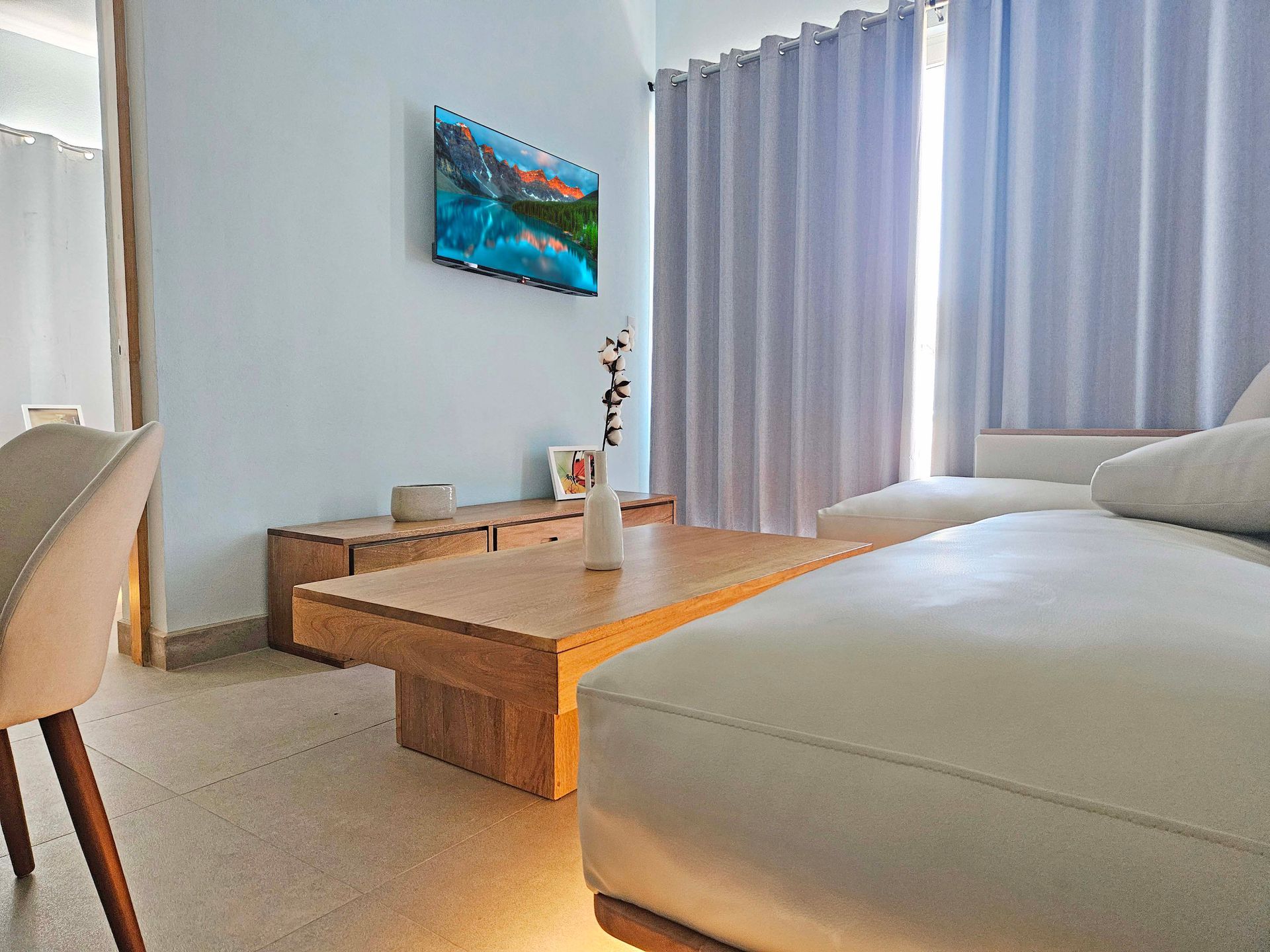 Living room with a light blue wall, white sofa, wooden coffee table, and a landscape painting.
