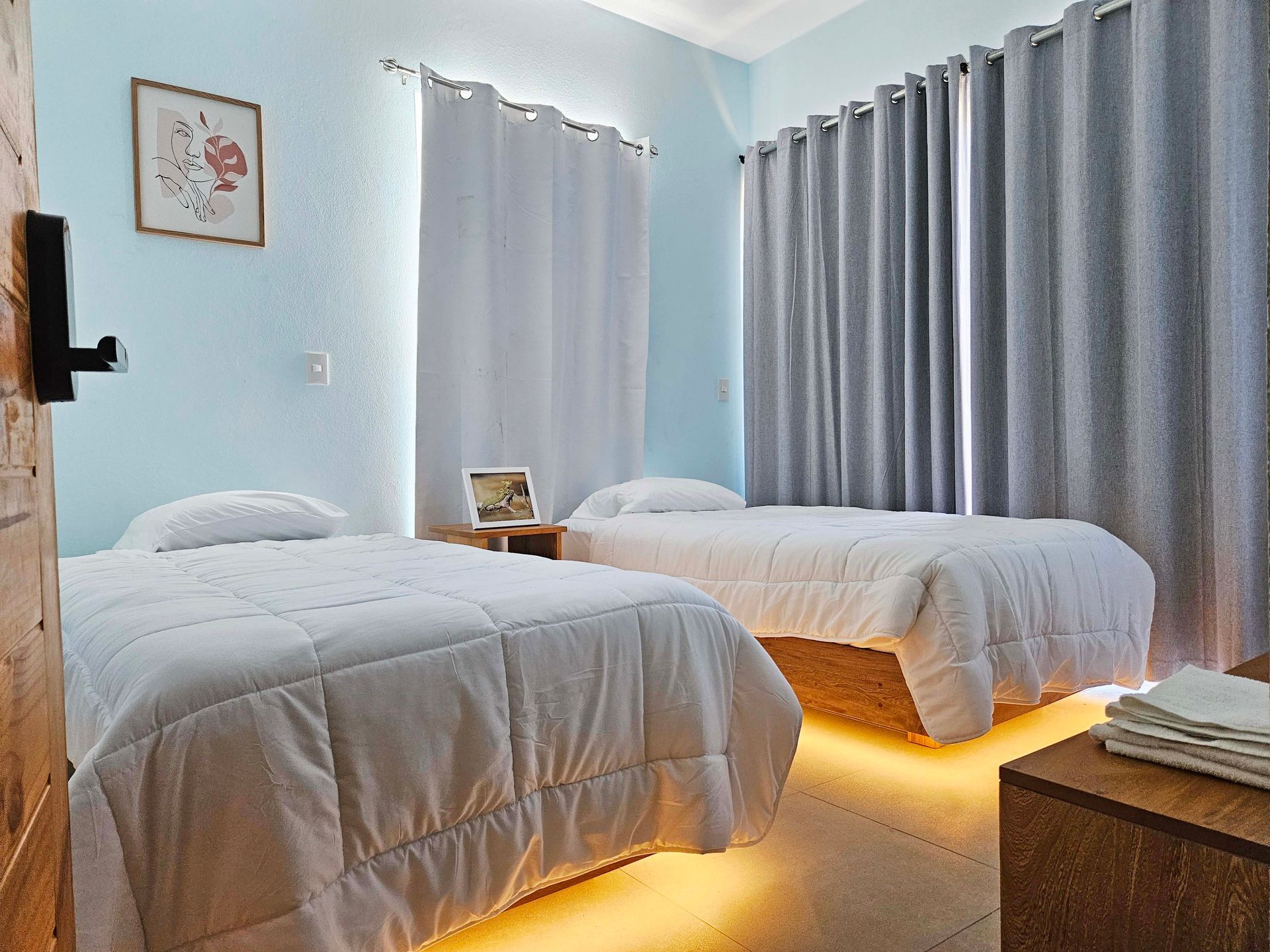 Two twin beds in a room with light blue walls, white bedding, and gray curtains.