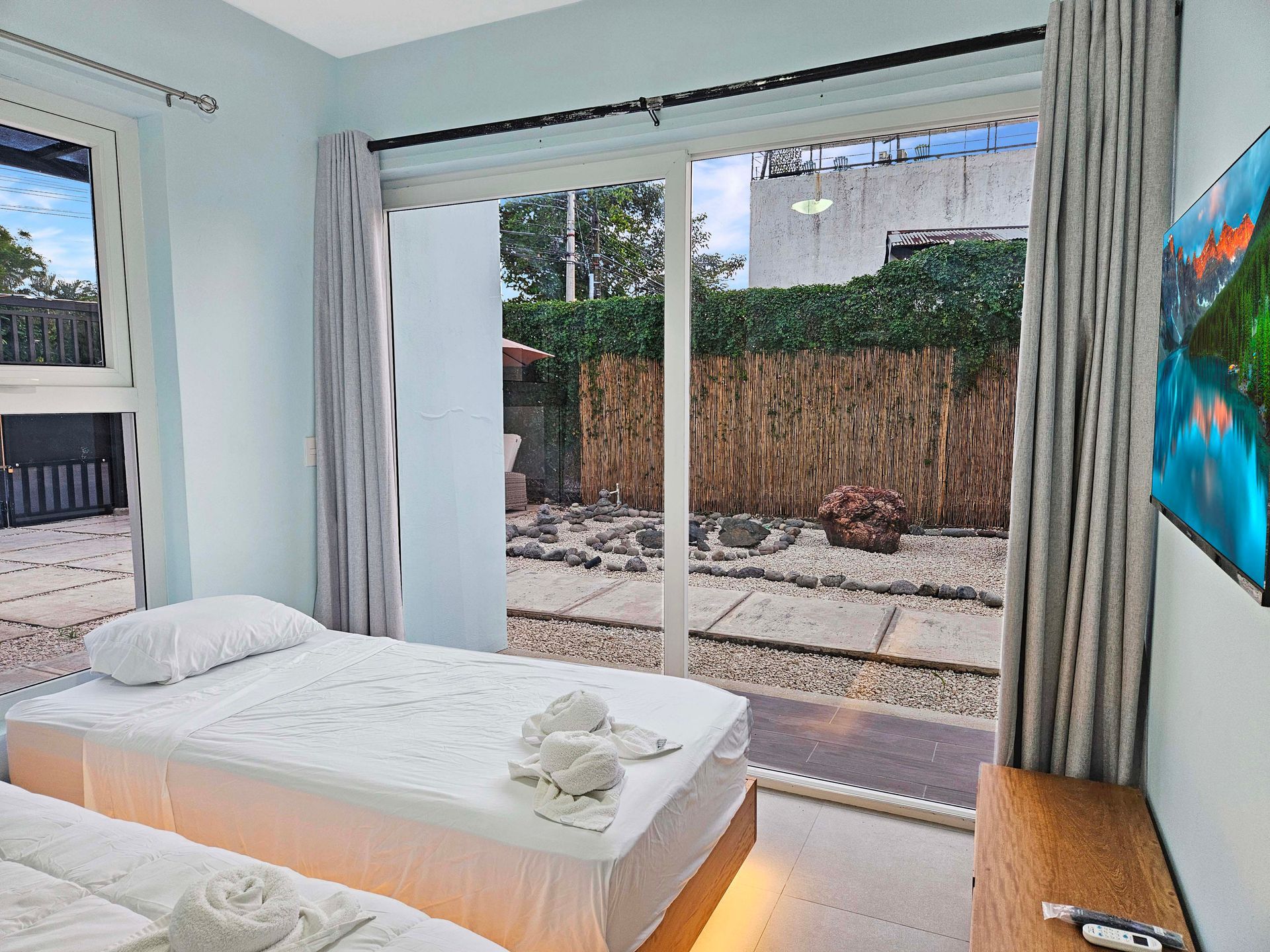 Bedroom with two twin beds, large window overlooking a yard, and a wall-mounted TV.