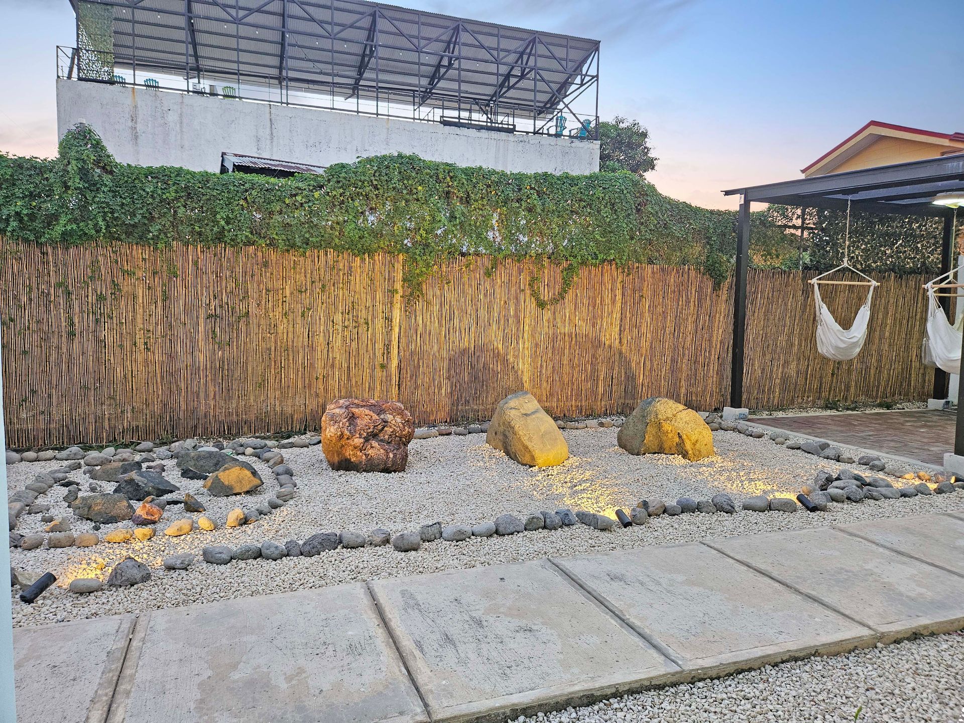 A backyard zen garden with rocks, a fire pit, and a reed fence. Solar panels on the roof.