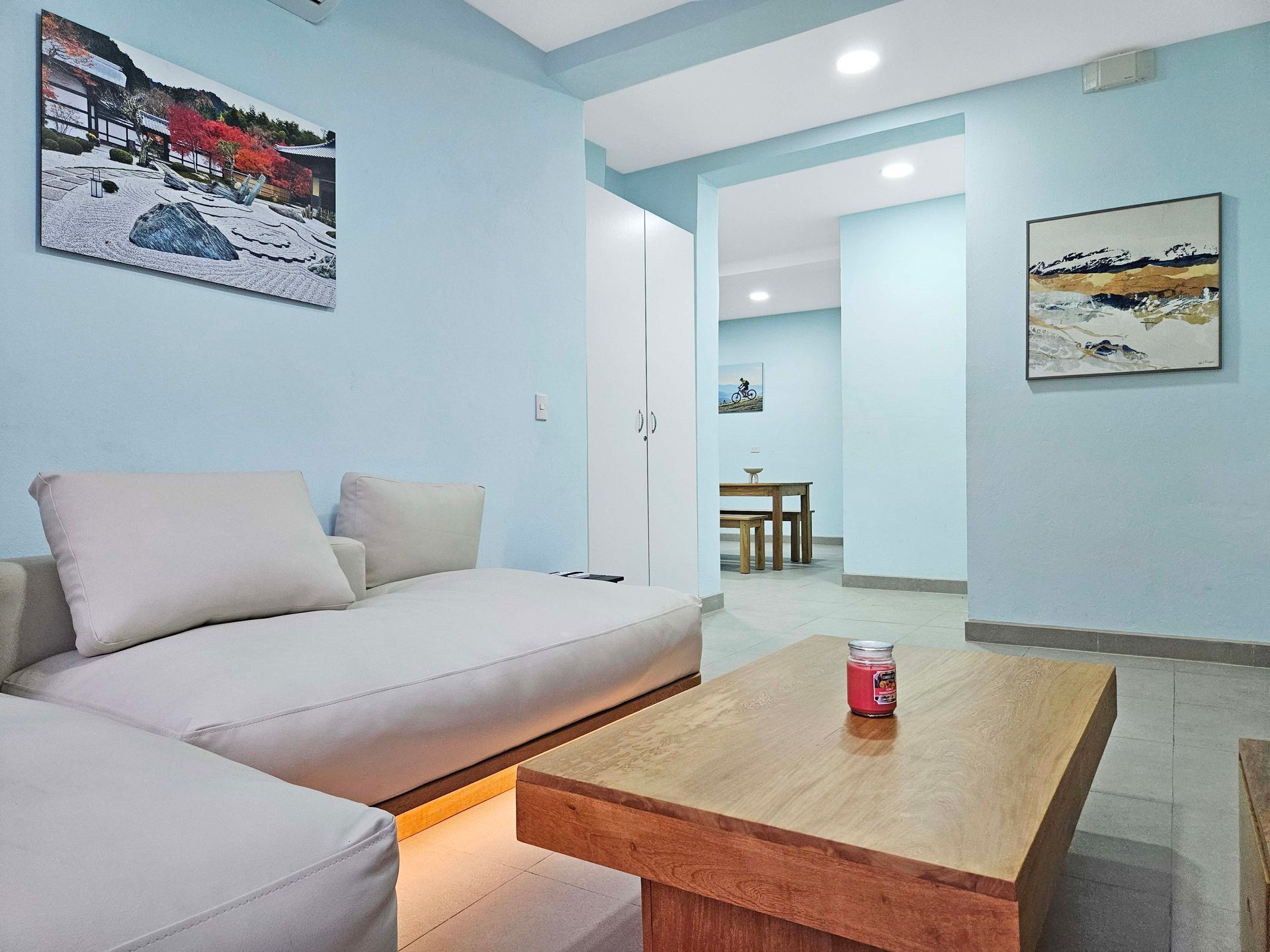 Living room with light blue walls, a white couch, wooden coffee table, and art.
