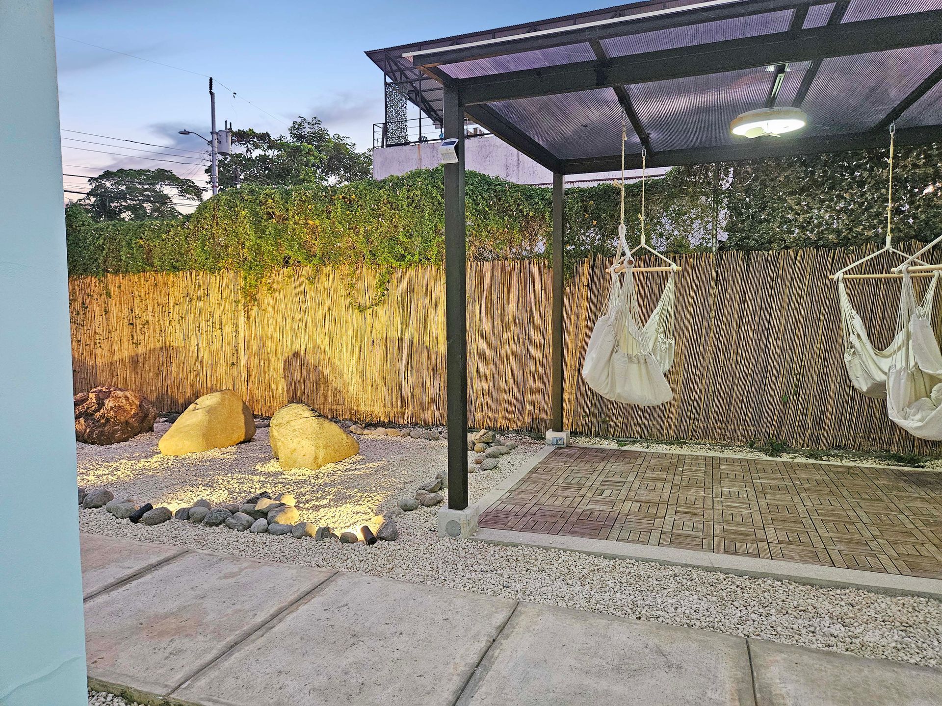 Outdoor seating area with swing chairs, a rock garden, and a bamboo fence.
