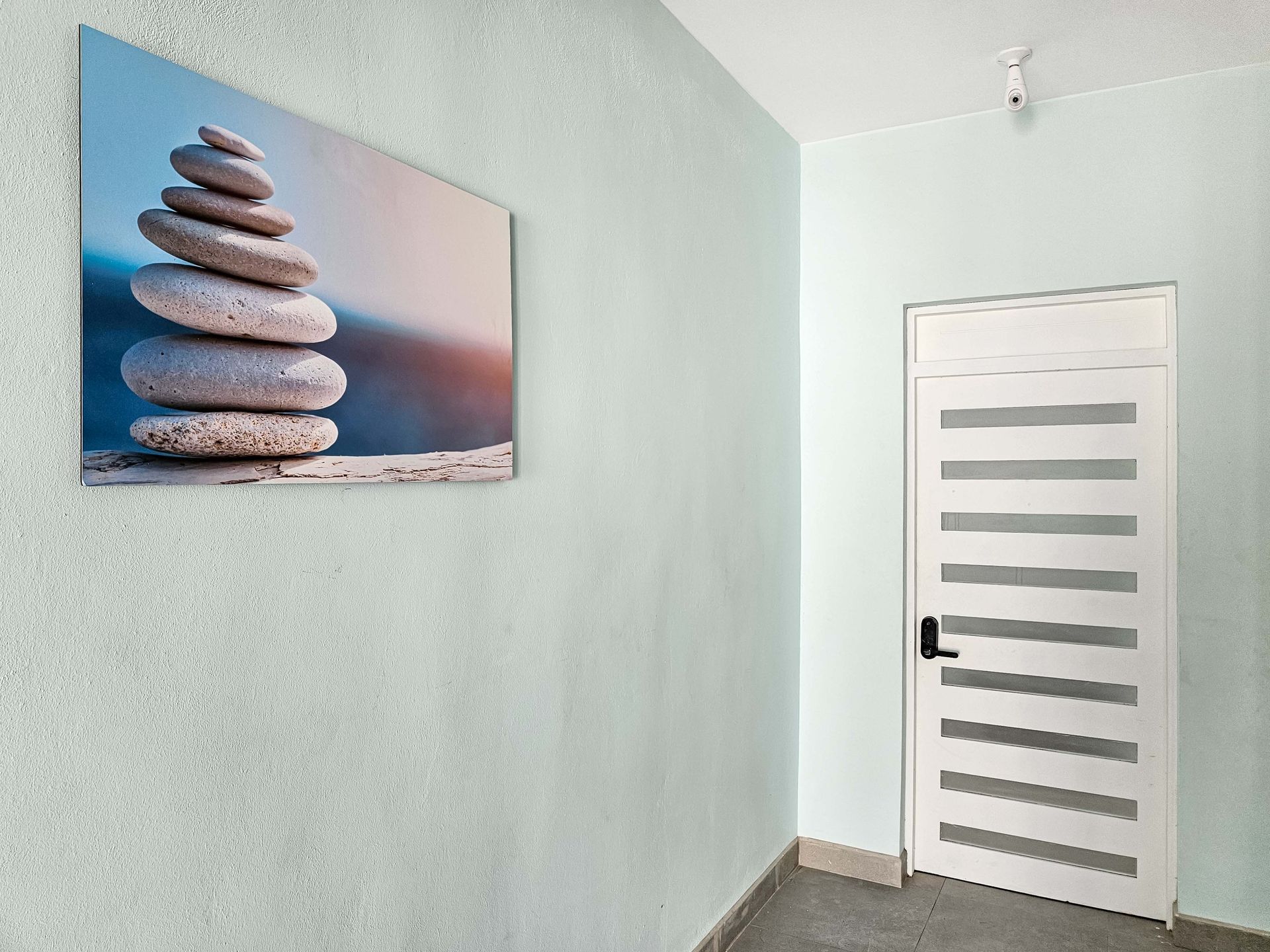 A hallway with a stacked stones artwork on a light blue wall. A white door is on the right.