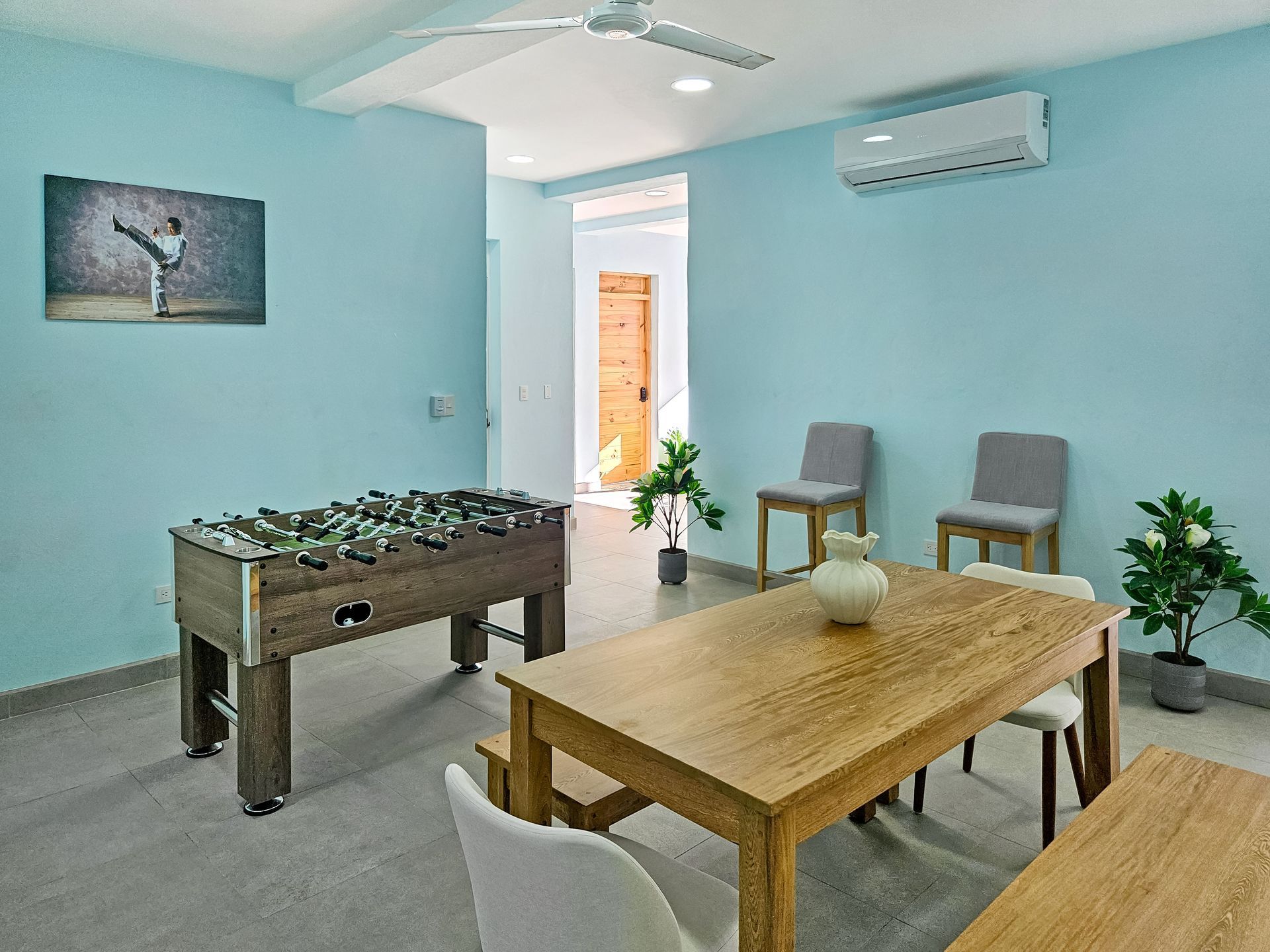 A light blue room with a foosball table, dining table, chairs, and an open doorway.