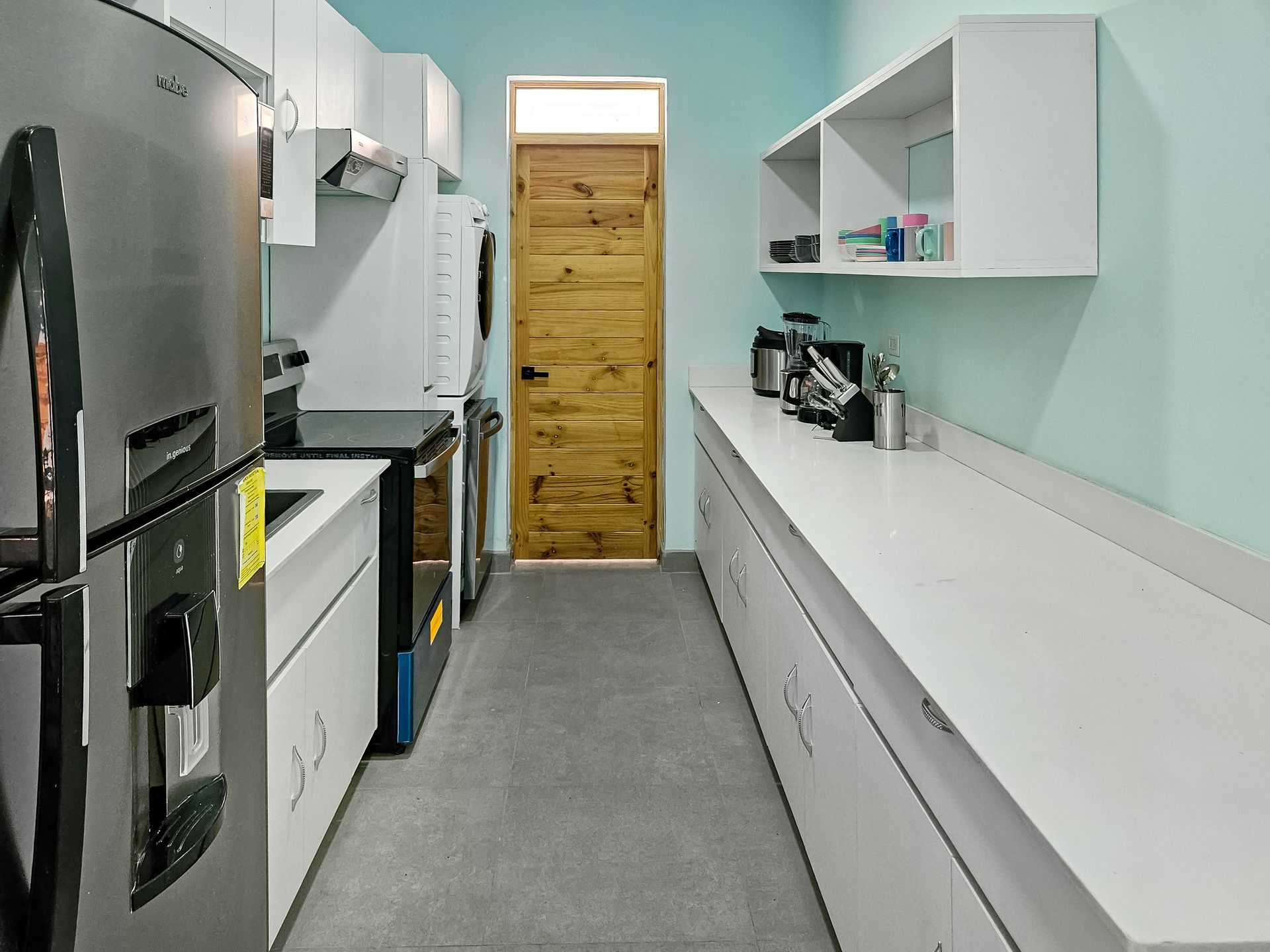 Narrow, modern kitchen with white cabinets, stainless steel appliances, and a wood door.