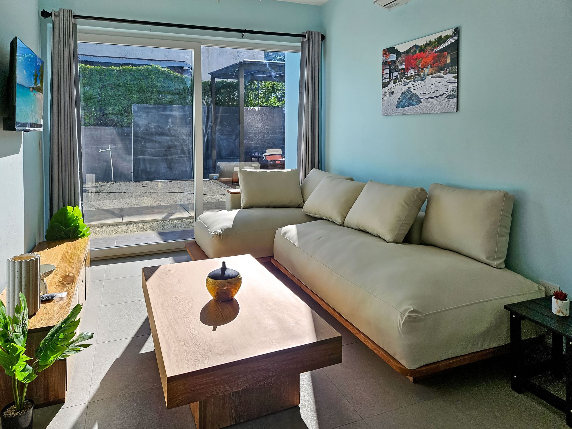 Living room with light blue walls, tan couch, wooden coffee table, and a sliding glass door to an outdoor area.