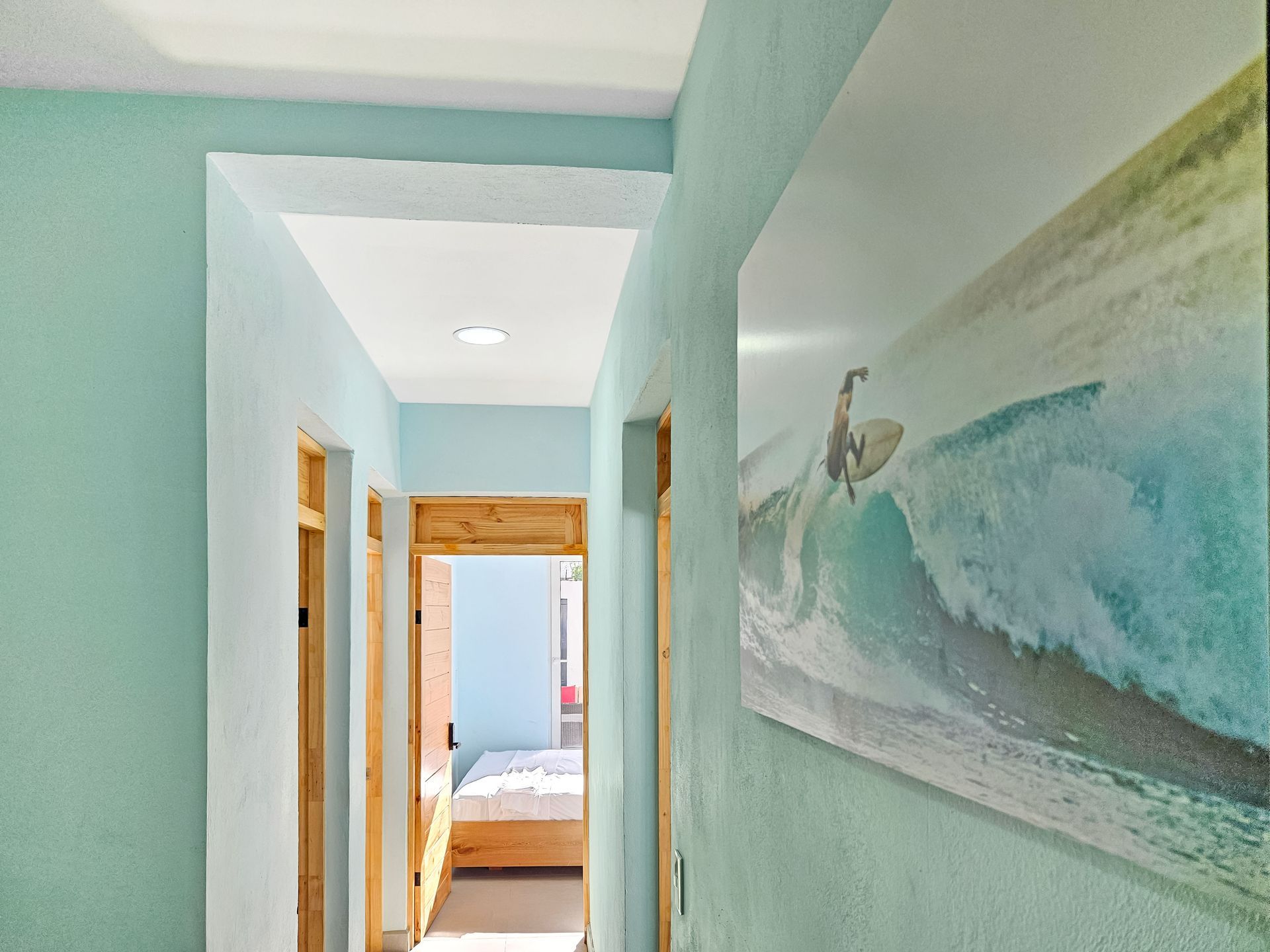 Hallway with turquoise walls, wooden door frames, and a surf art print.