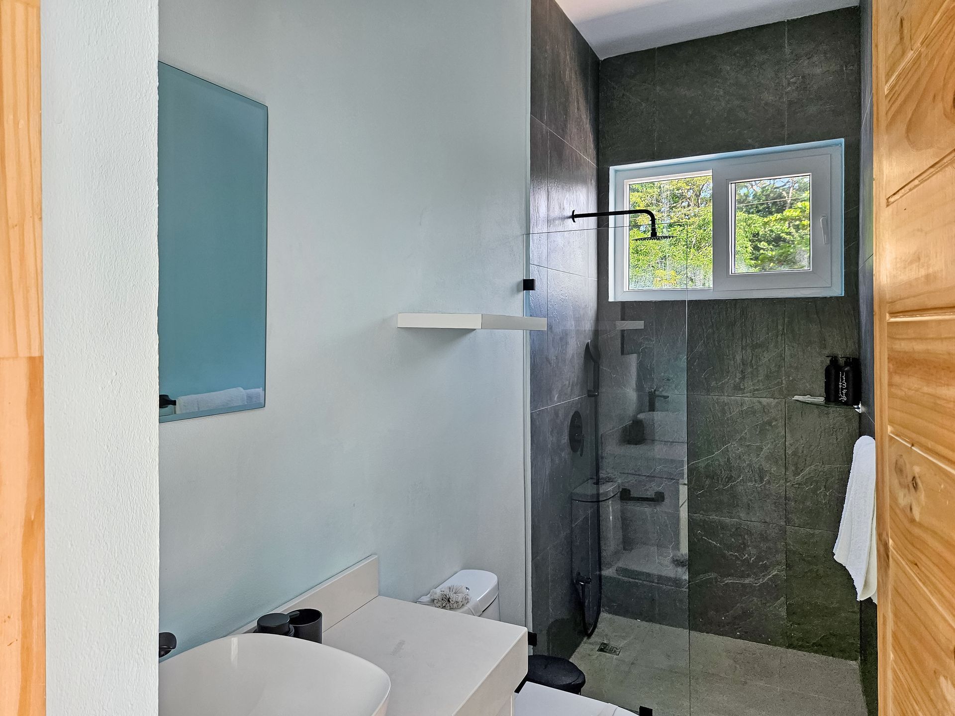 Bathroom with a tiled shower, white sink, and small window looking outside.
