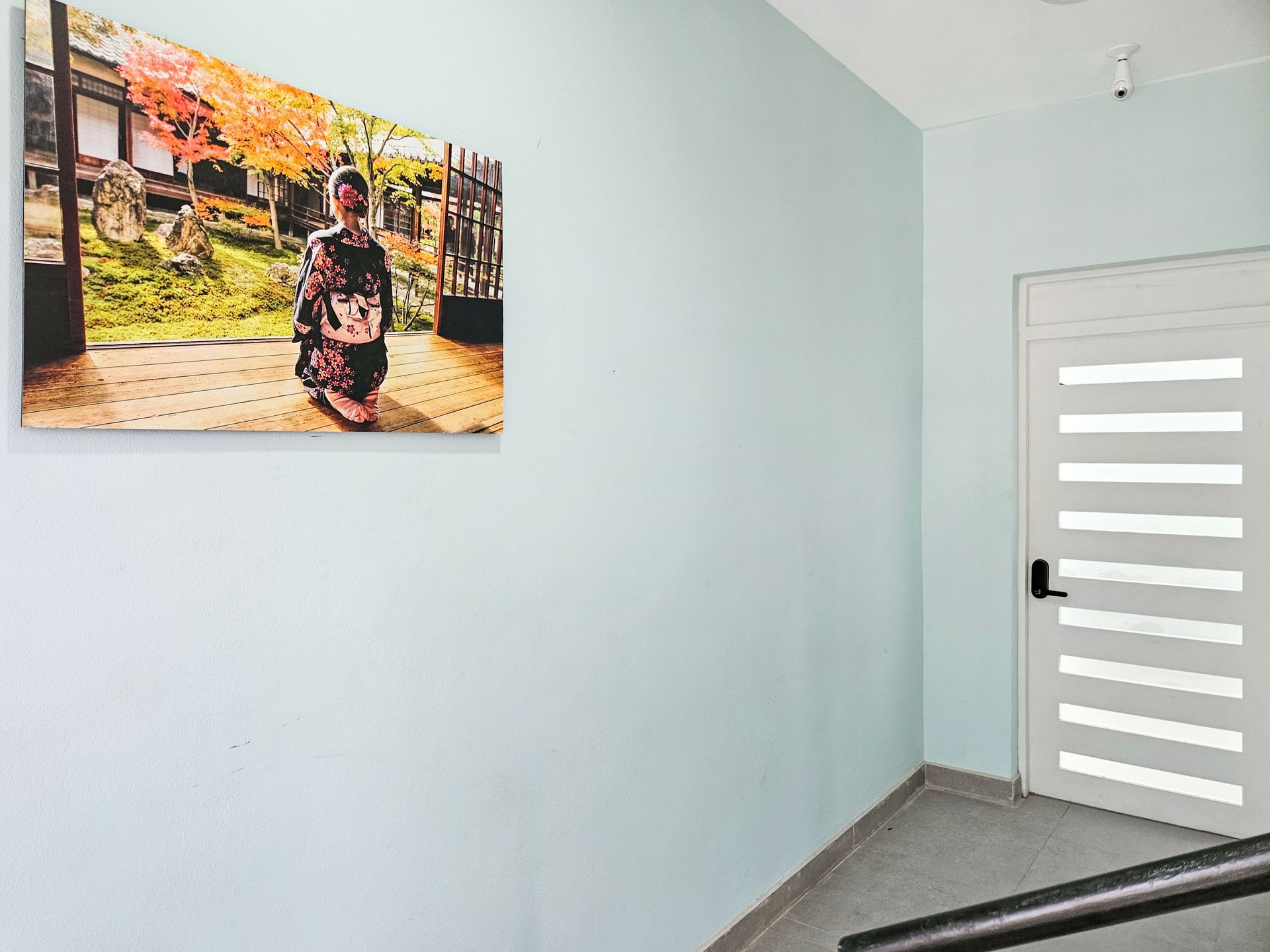Light blue wall with Japanese art print, white door, and a staircase with a black handrail.