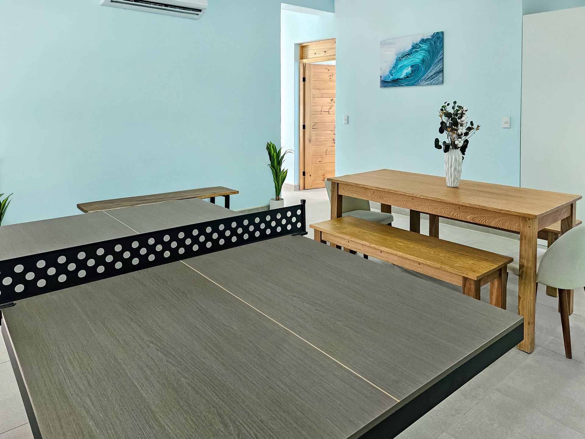 Ping pong table in a room with a dining table and wooden door; pale blue walls.