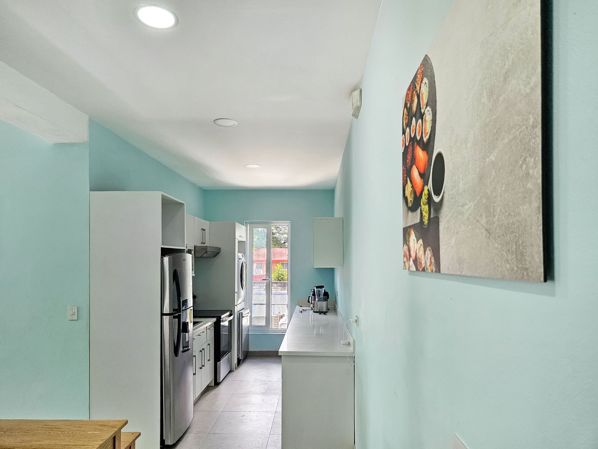 A narrow kitchen with light blue walls, white cabinets, and stainless steel appliances.