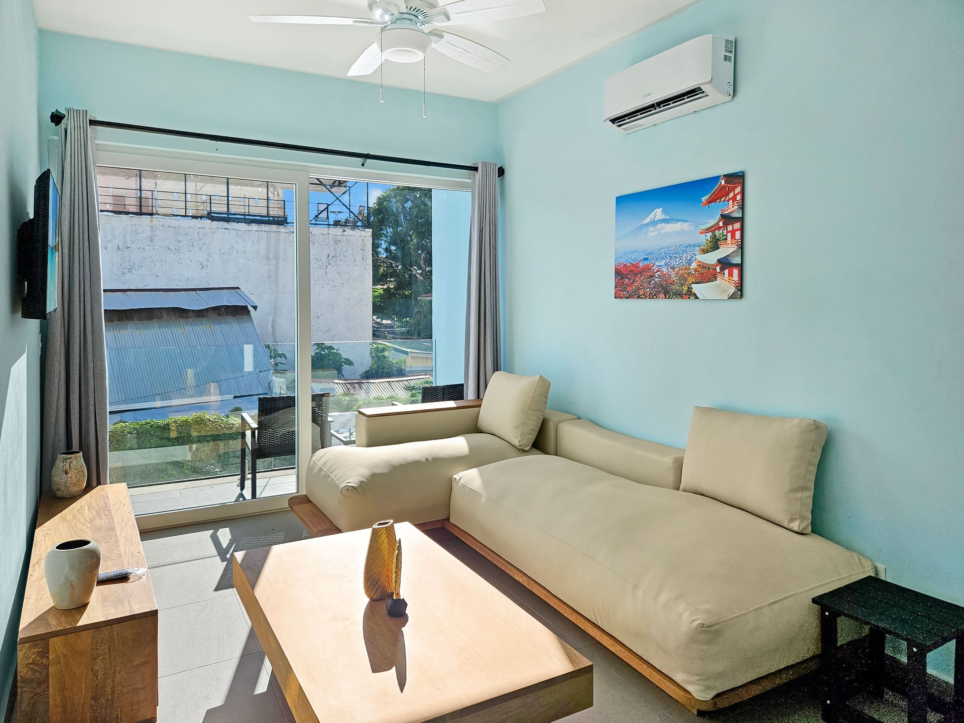 Living room with light blue walls, beige sectional sofa, sliding glass door, and wooden coffee table.