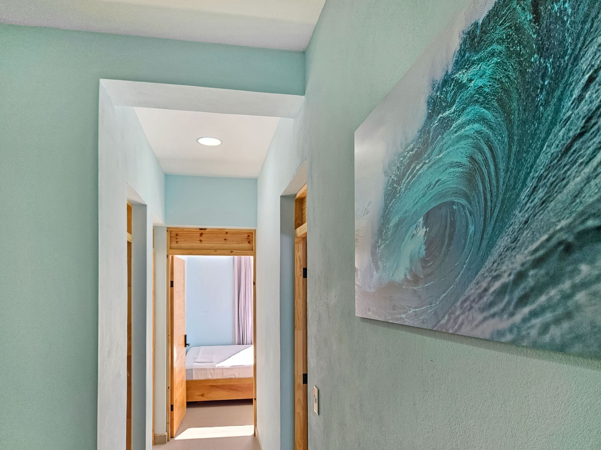 Hallway painted light blue, with a wave art piece and a doorway to a bedroom.