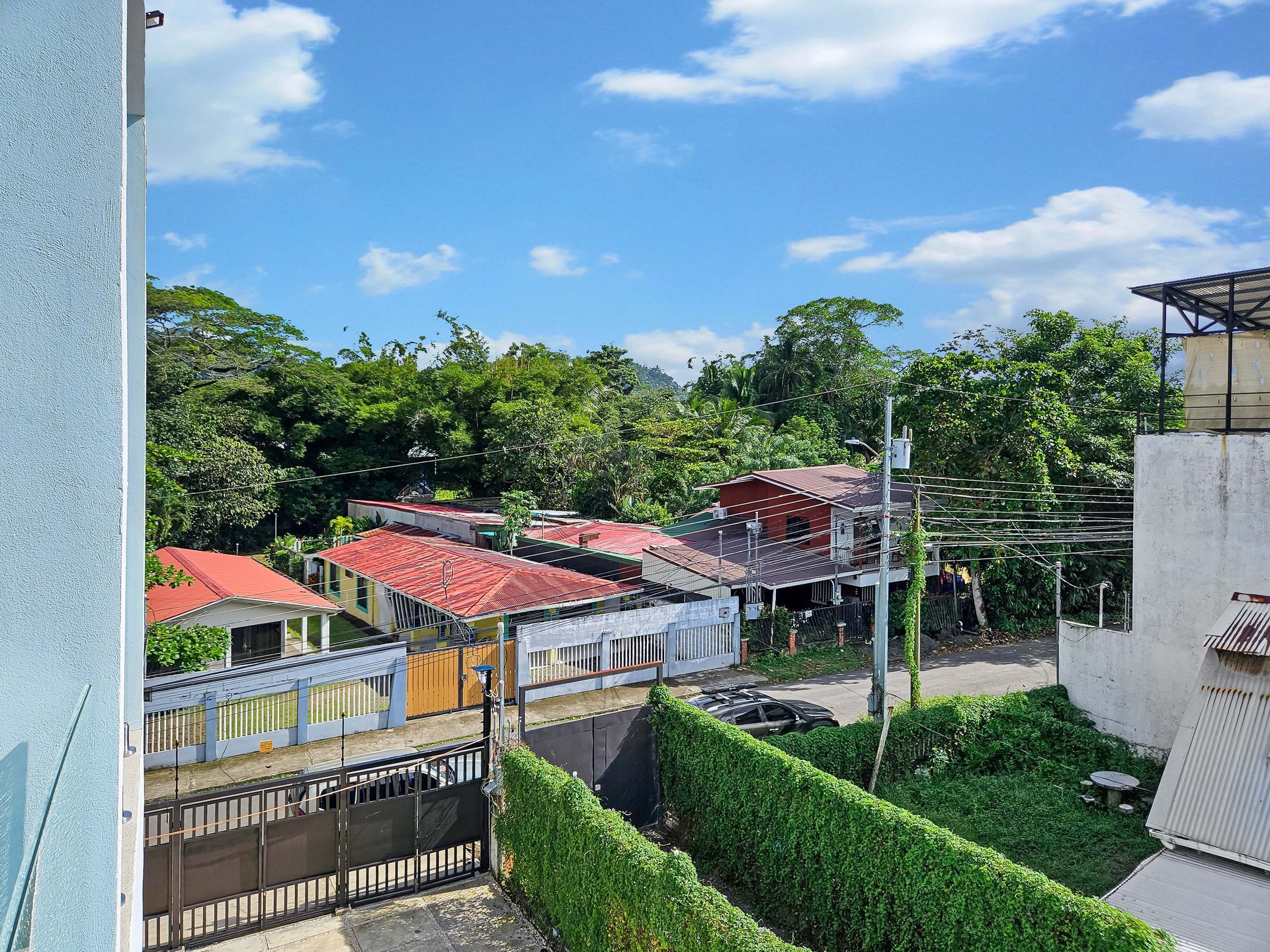 View of houses with red and brown roofs surrounded by greenery under a partly cloudy sky.