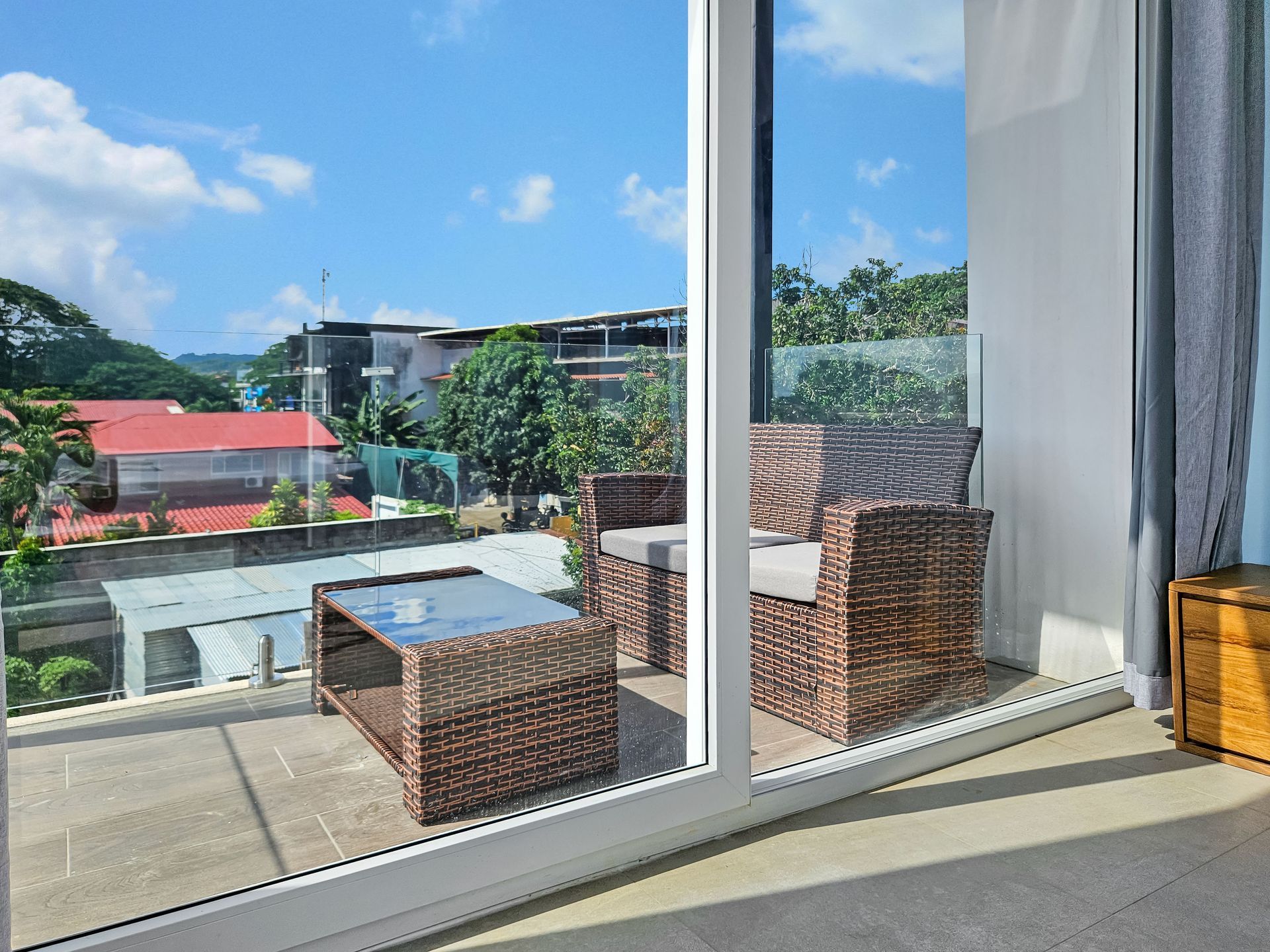 Balcony with wicker furniture overlooking a cityscape on a sunny day.