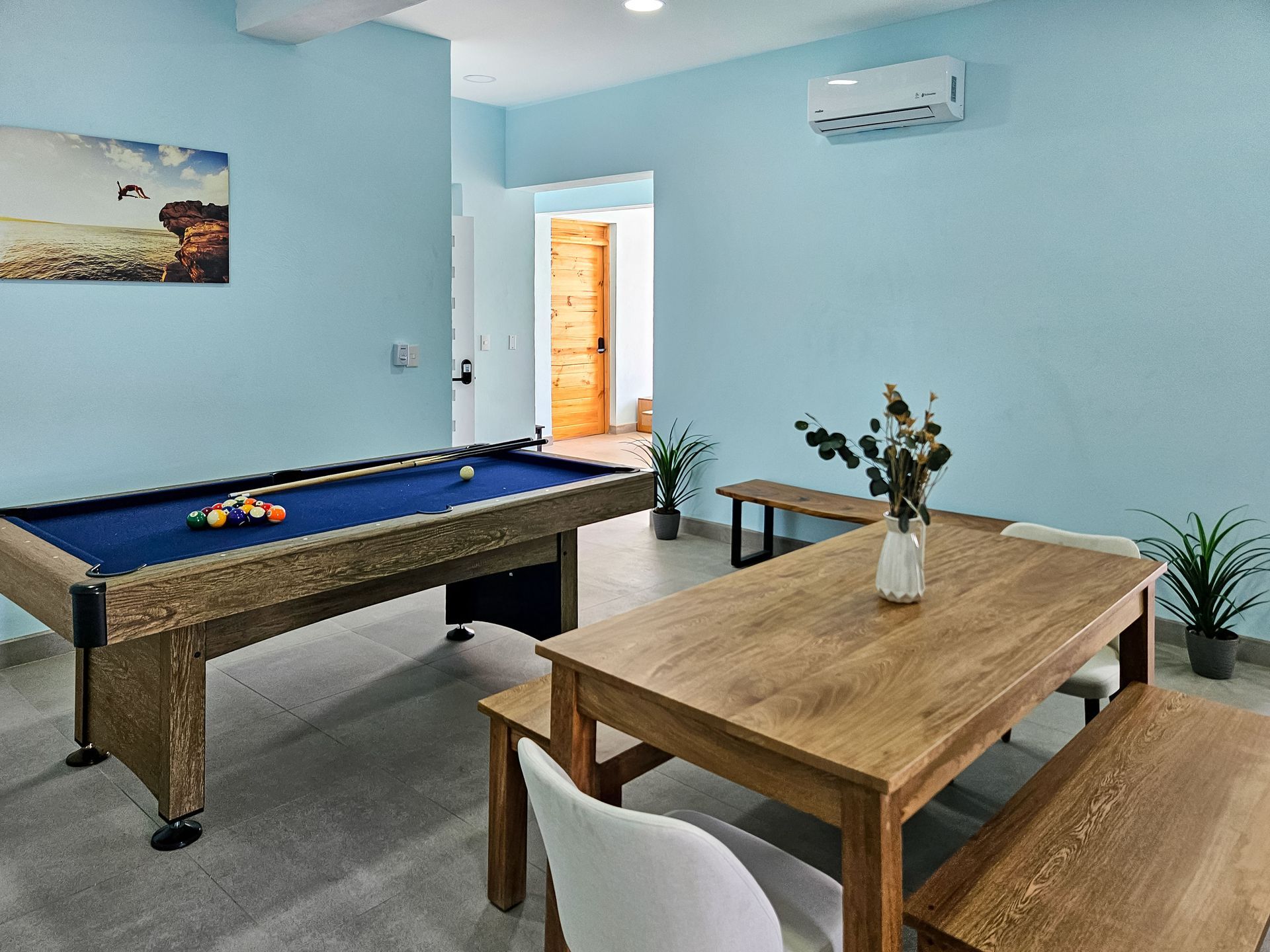 A game room with a pool table, wooden table and benches, and blue walls.
