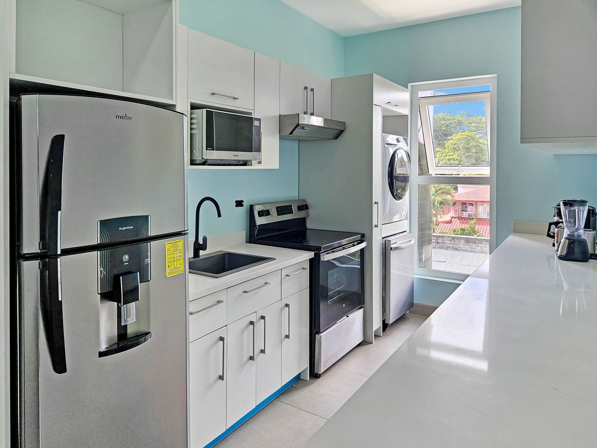 Modern kitchen with stainless steel appliances, white cabinets, and a window with a view.
