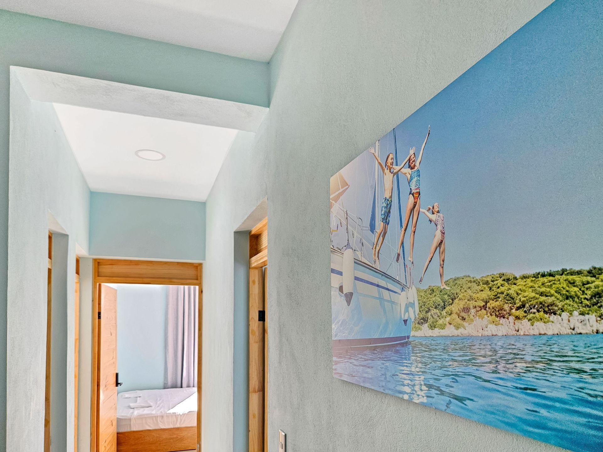 Hallway with a blue wall, framed photo of people jumping from a boat, and wooden door frames.