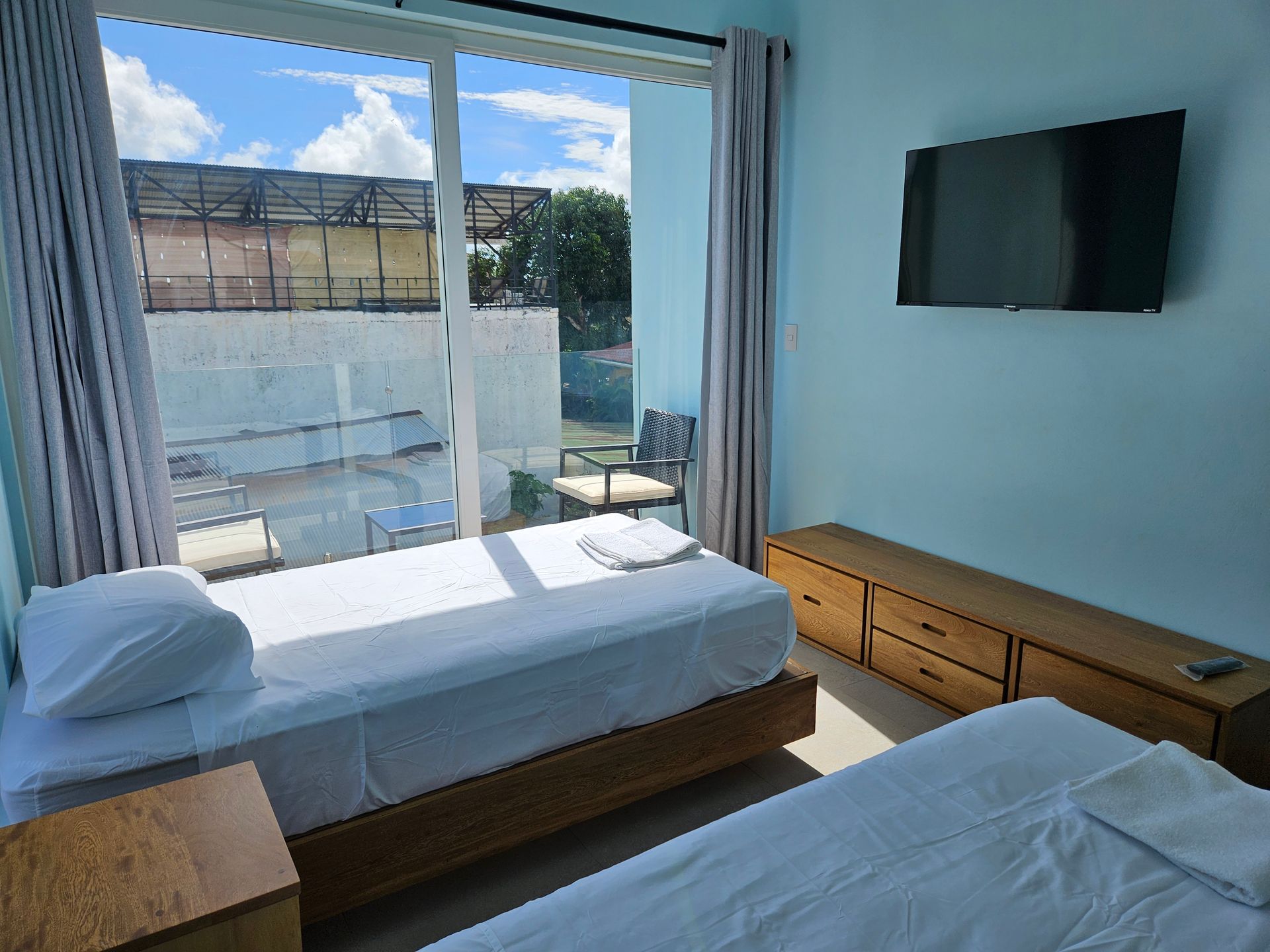 Two twin beds in a light blue room with a balcony view and mounted TV.