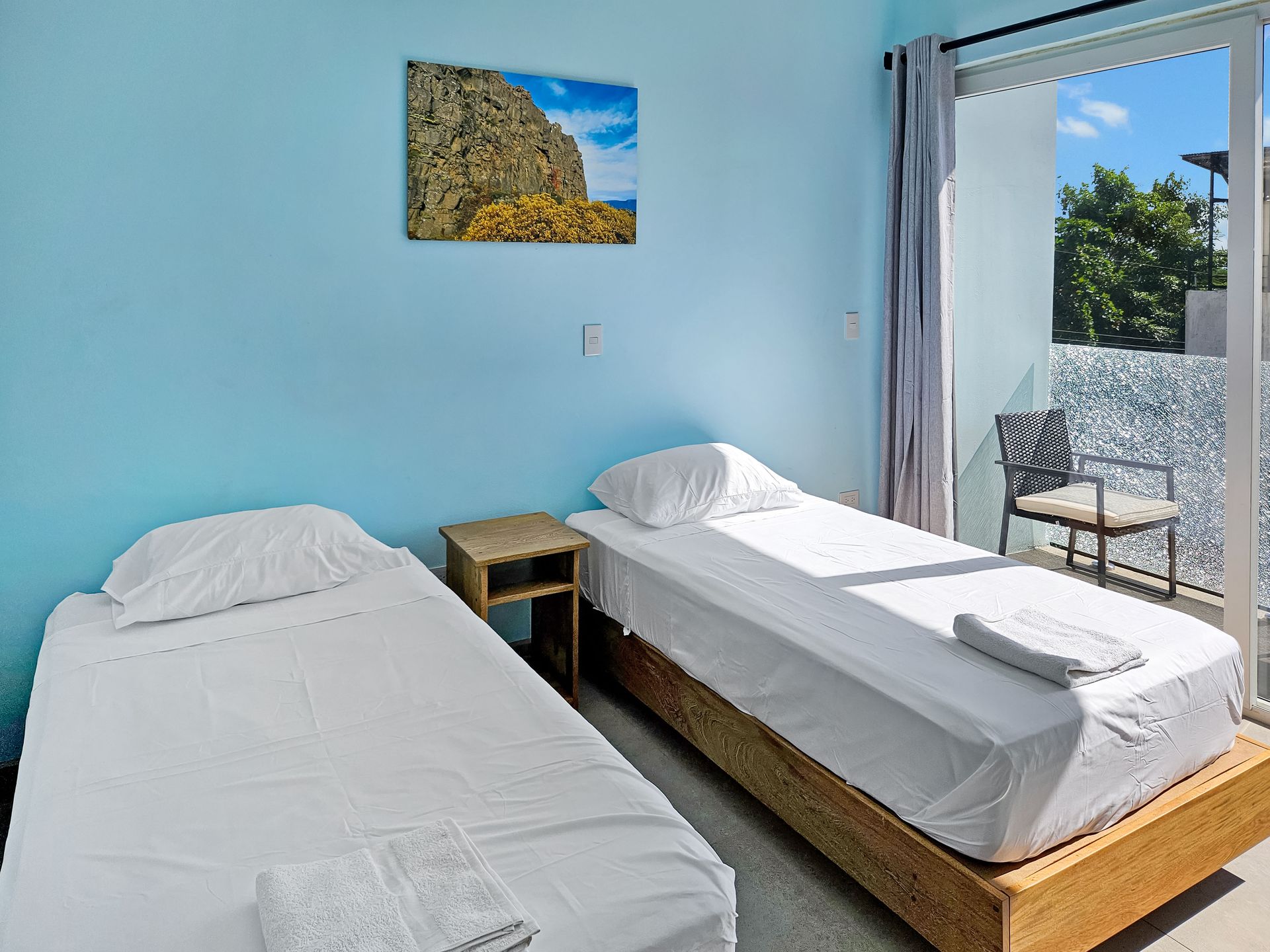 Two twin beds in a room with blue walls, a small table, and a balcony with a chair.