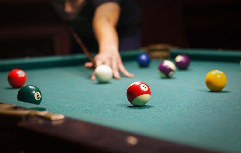 Person playing pool, cue stick over a green felt table, multiple colored balls.