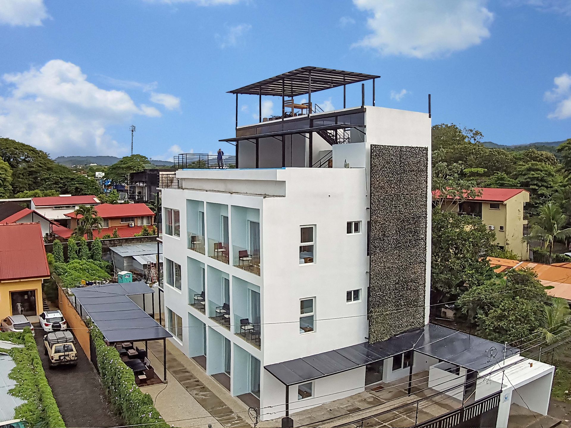White multi-story hotel with balconies, rooftop deck, and stone accent wall, surrounded by neighborhood.